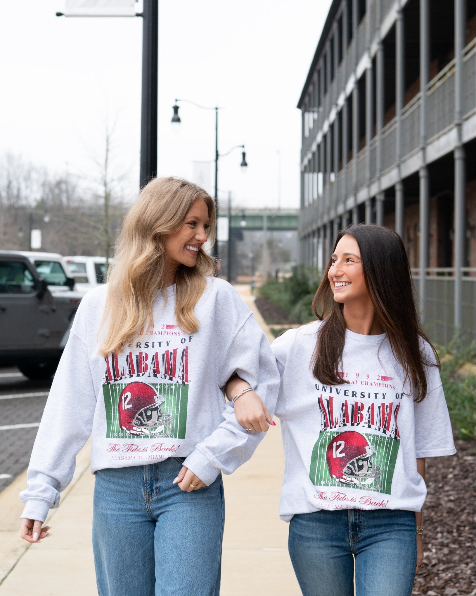 Two women wearing matching University of Alabama sweatshirts walking outdoors.
