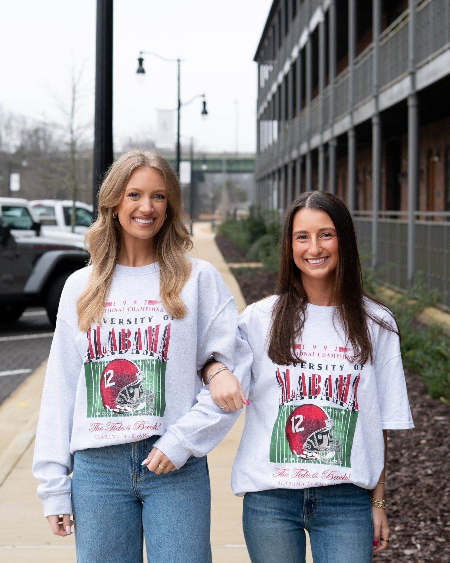 Two women wearing matching sweatshirts with a graphic design on a street.