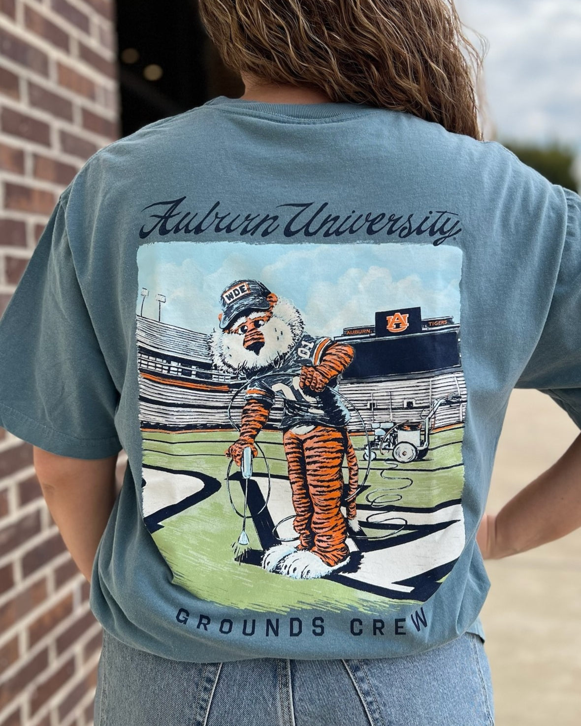 Auburn University Aubie Grounds Crew Ice Blue Comfort Colors T-Shirt with an image of Aubie the Tiger wearing a hat and painting the turf on the football field