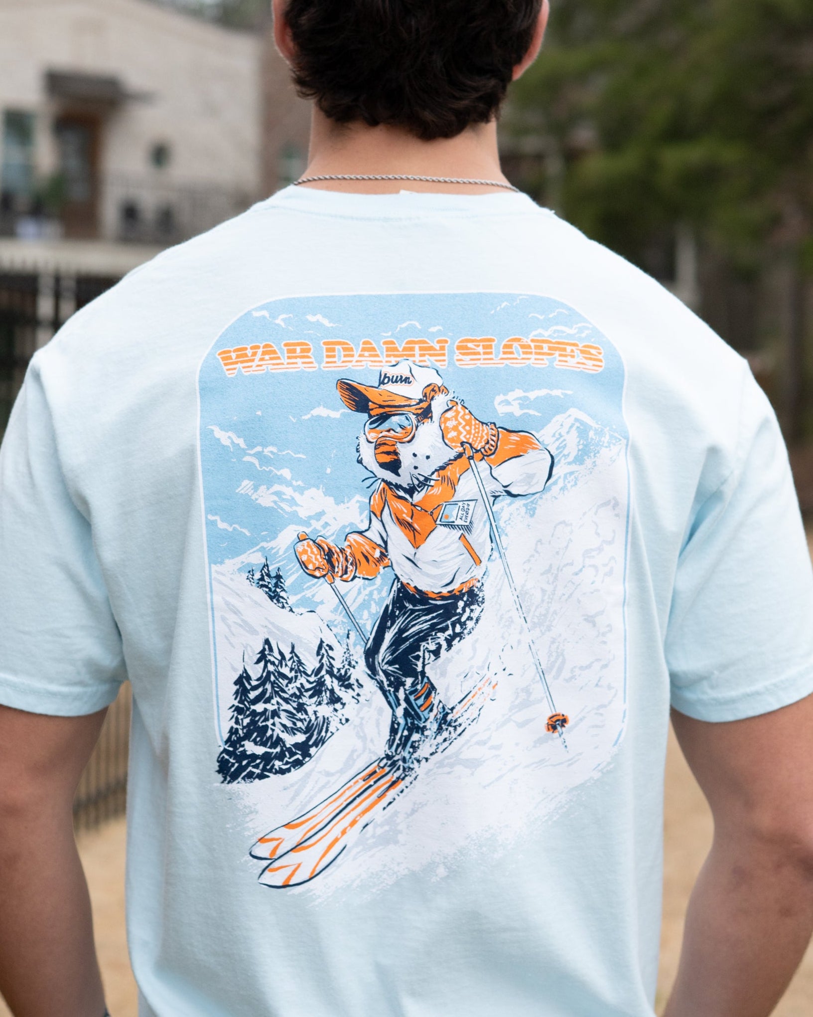 Auburn University Aubie Snow Skiing Chambray Comfort Colors T-Shirt with text "War Damn Slopes" above an image of Aubie in a ski outfit skiing down a snow-covered mountain