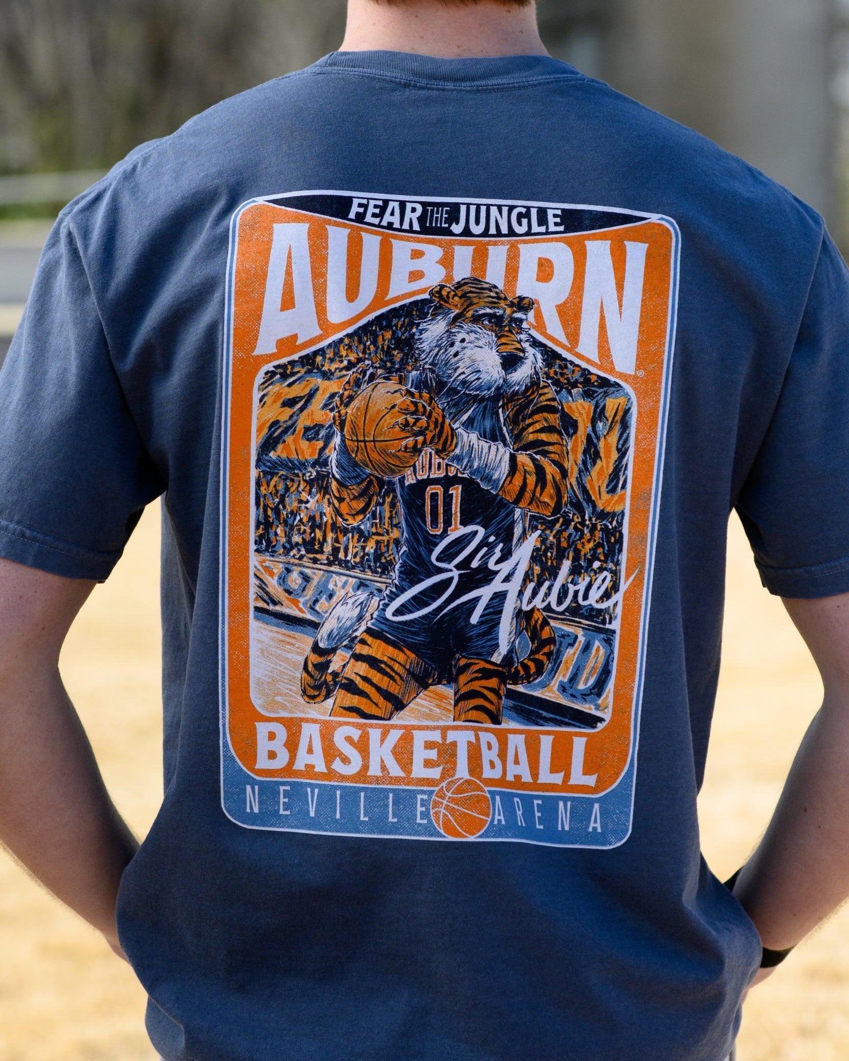 Auburn University Dark Blue T-Shirt with a basketball card style design featuring Aubie dribbling a basketball down the court in between text “Fear the Jungle Auburn” and “Basketball Neville Arena” and with an autograph from “Sir Aubie”