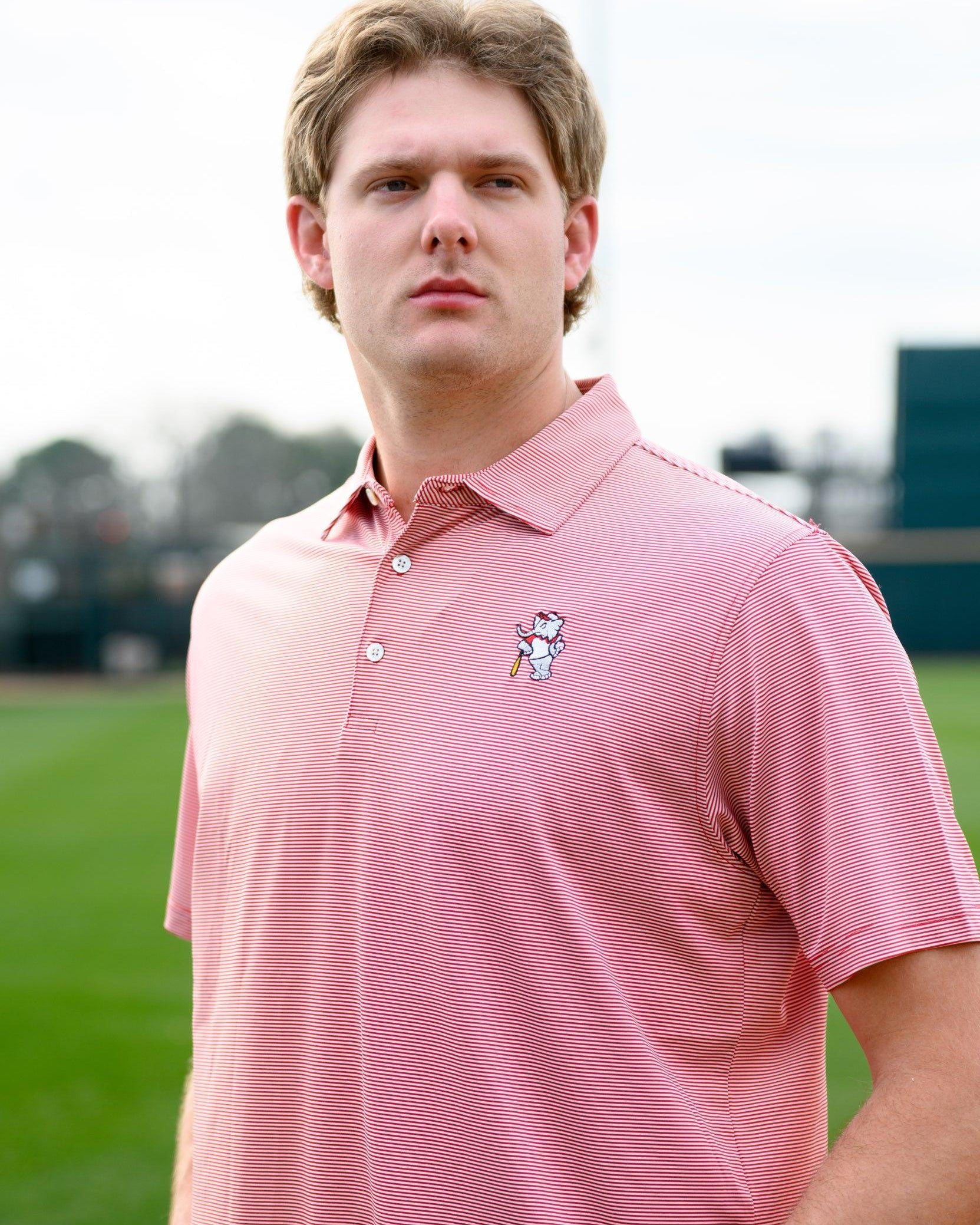 University of Alabama Men's Crimson Stripe Performance Polo with an embroidered image of Big Al in a baseball uniform leaning on a baseball bat