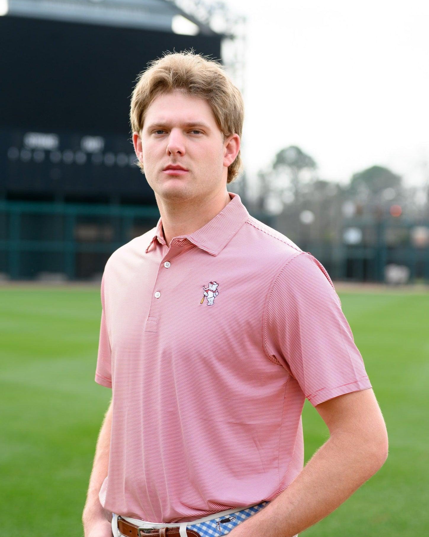 University of Alabama Men's Crimson Stripe Performance Polo with an embroidered image of Big Al in a baseball uniform leaning on a baseball bat