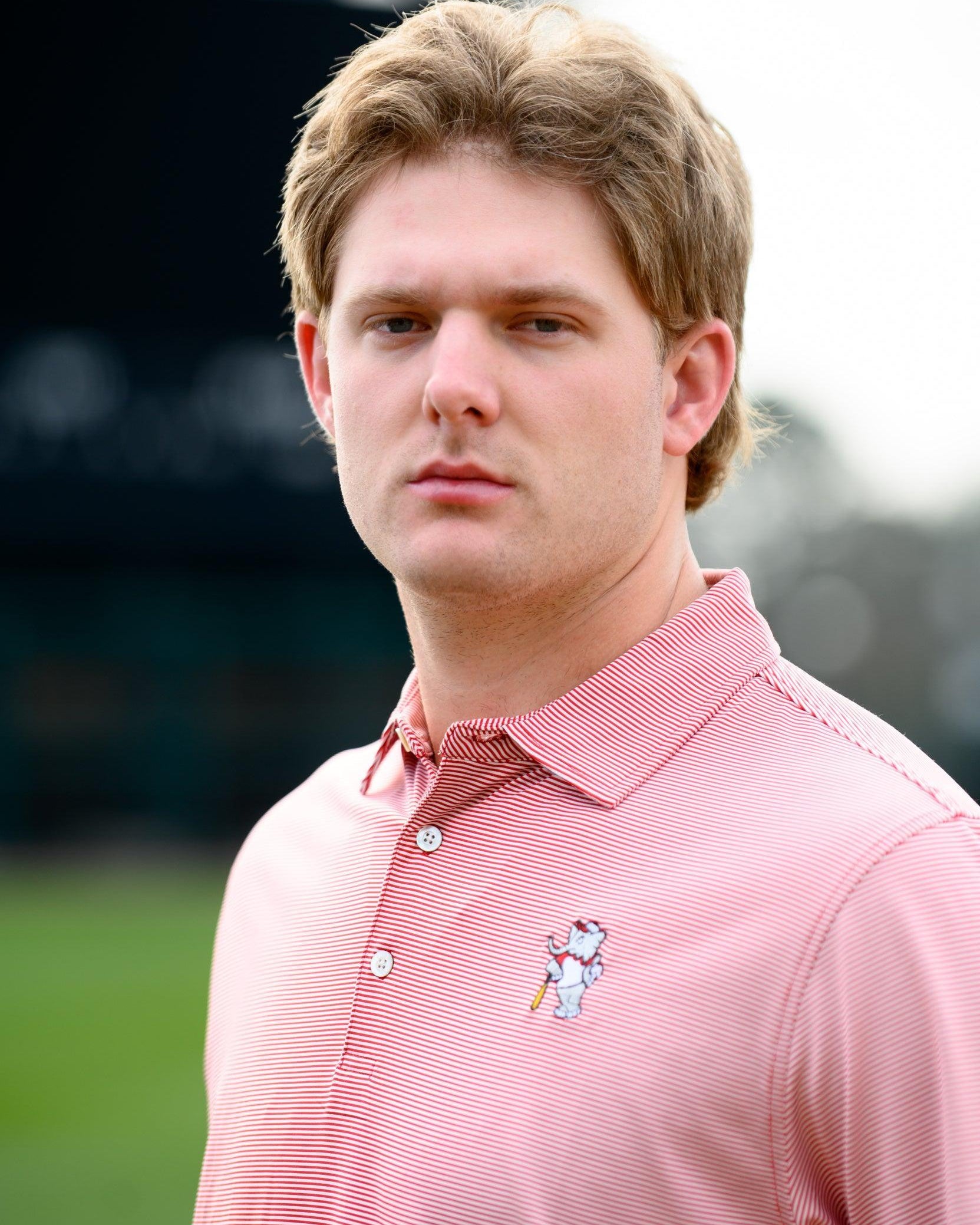 University of Alabama Men's Crimson Stripe Performance Polo with an embroidered image of Big Al in a baseball uniform leaning on a baseball bat