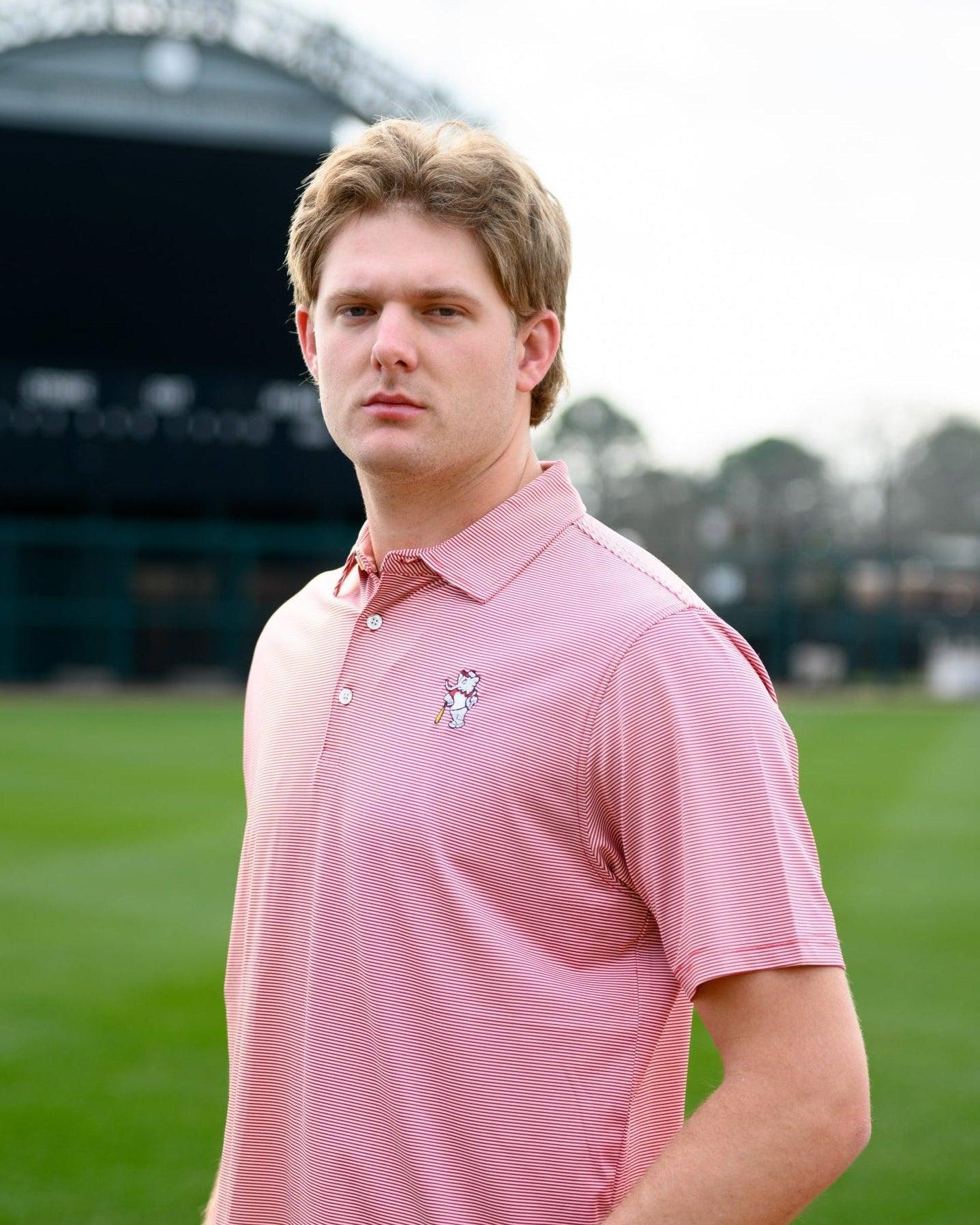 University of Alabama Men's Crimson Stripe Performance Polo with an embroidered image of Big Al in a baseball uniform leaning on a baseball bat