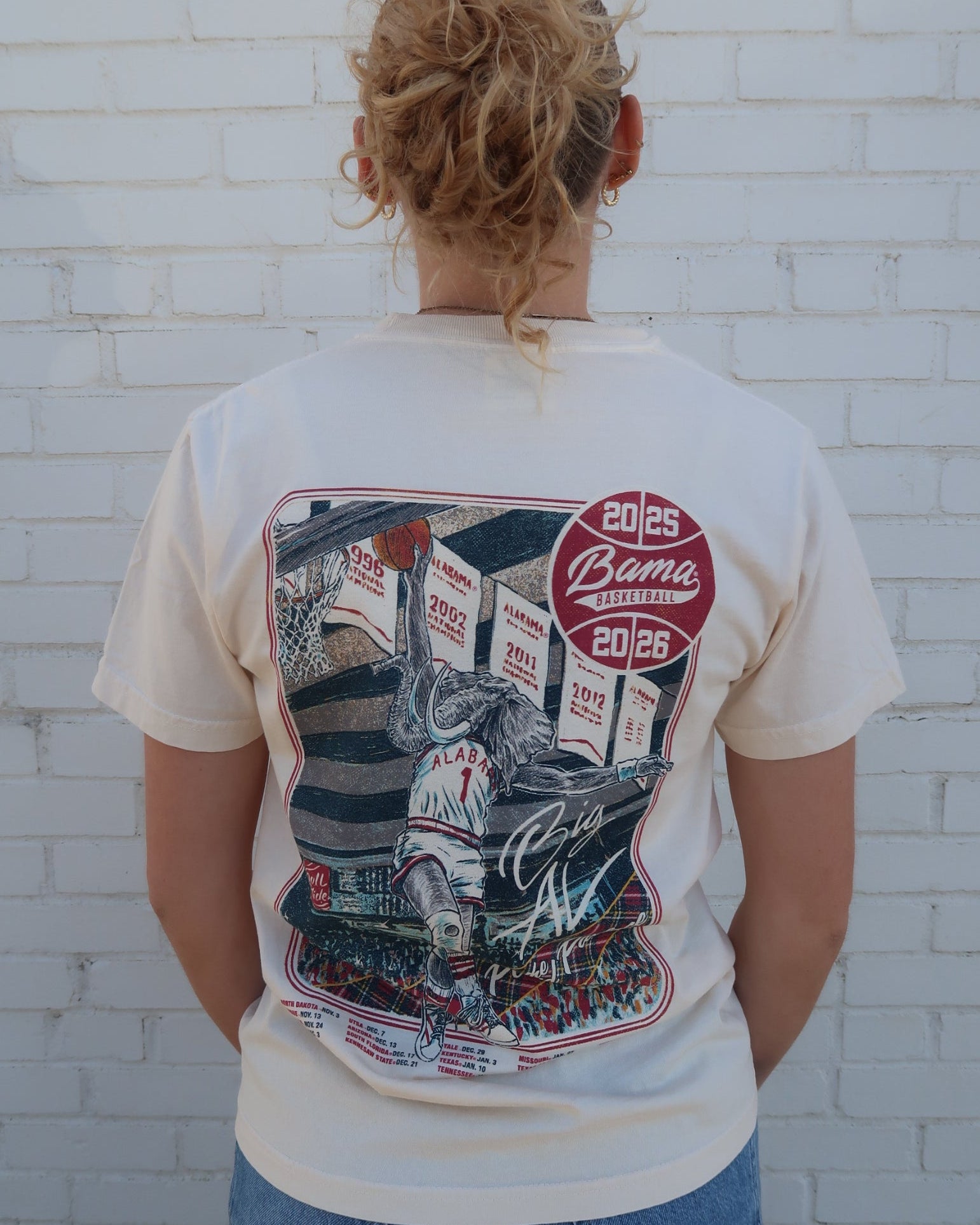 University of Alabama Ivory Shirt with an illustration of Big Al dunking a basketball next to text “Big Al” and “the Plaid Palace” above the 2025 Basketball Schedule