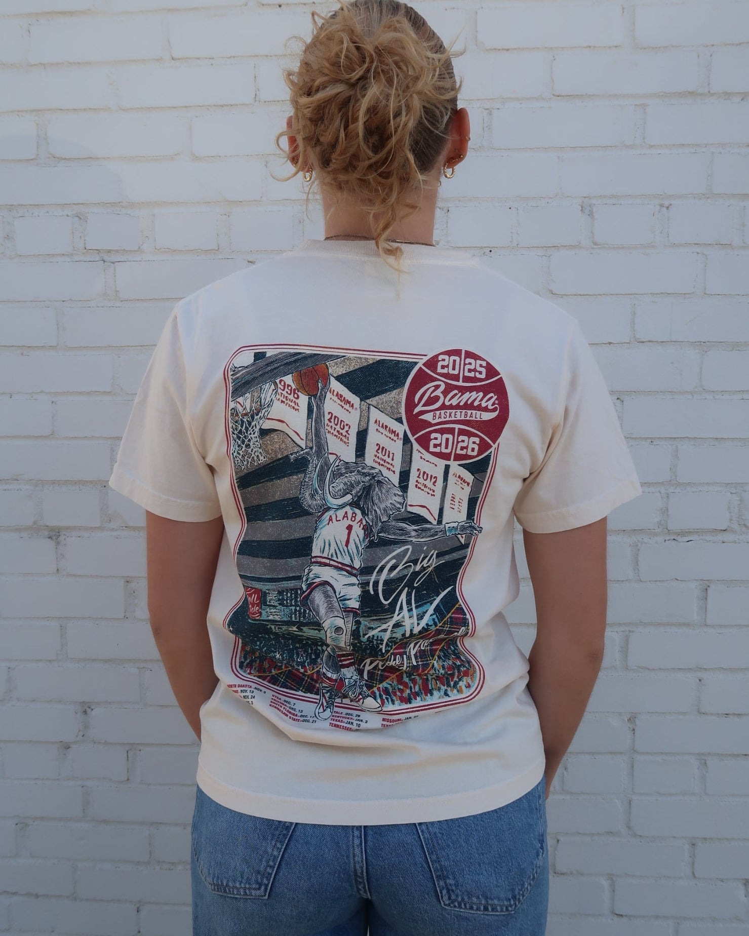University of Alabama Ivory Shirt with an illustration of Big Al dunking a basketball next to text “Big Al” and “the Plaid Palace” above the 2025 Basketball Schedule
