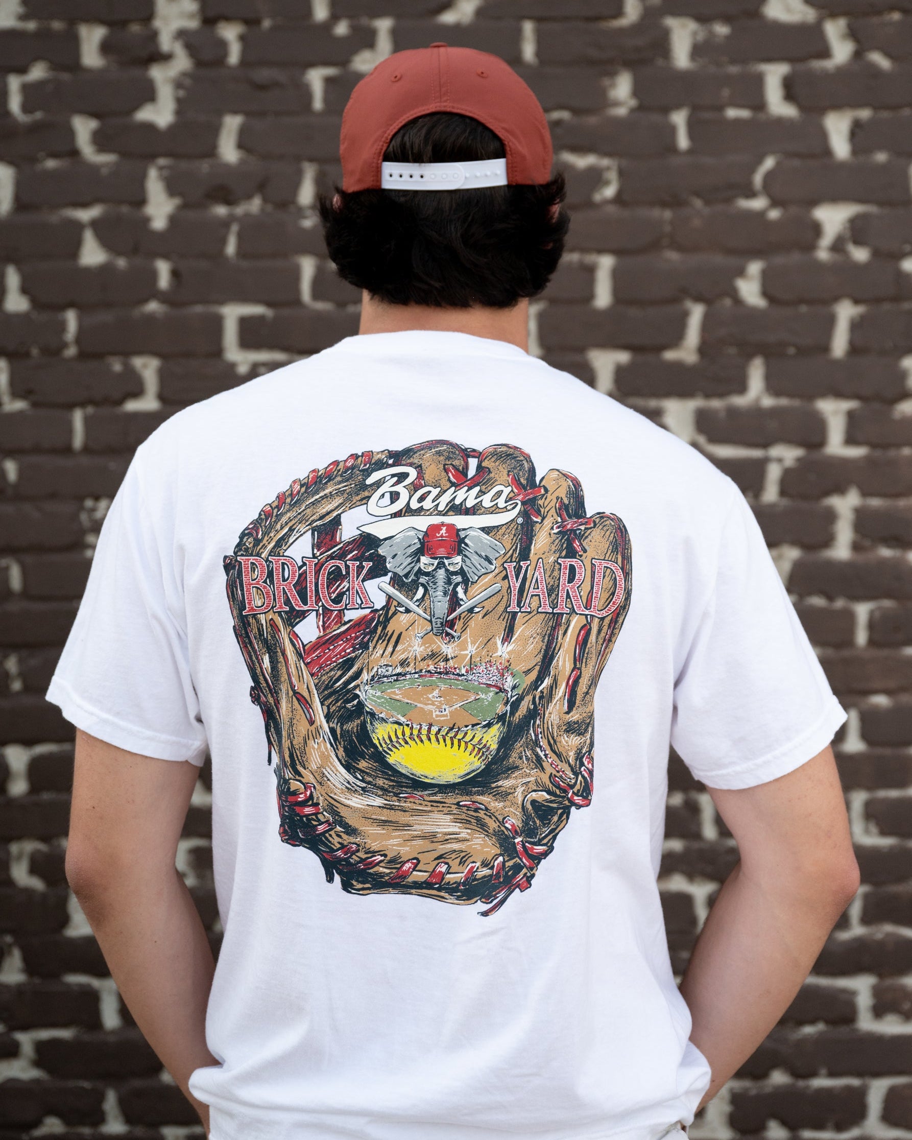 University of Alabama Bama Brick Yard White Comfort Colors T-Shirt with an image of a baseball glove catching a baseball field beneath the text "Bama Brick Yard"
