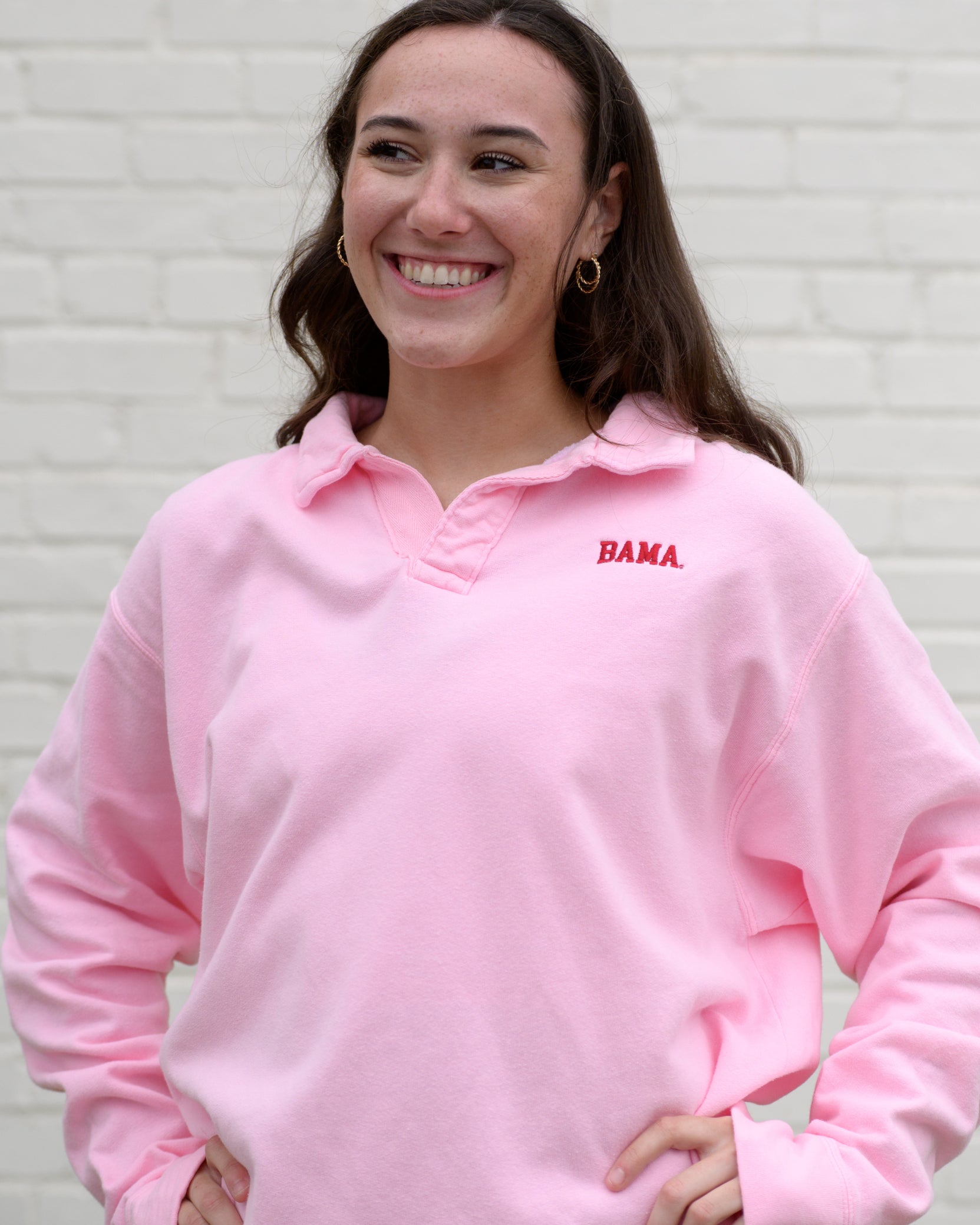 Woman wearing a pink collared sweatshirt with 'BAMA' embroidered in crimson on it.