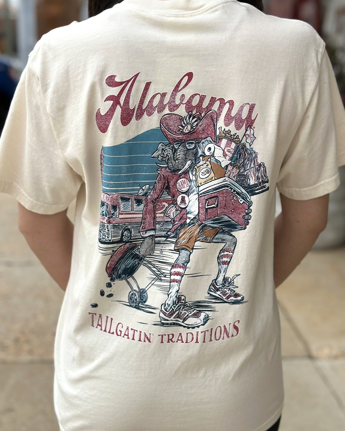 University of Alabama Cream Big Al Tailgate Comfort Colors T-Shirt with an image of Big Al in Gameday Gear with a cooler and a grill above text "Tailgatin' Traditions"
