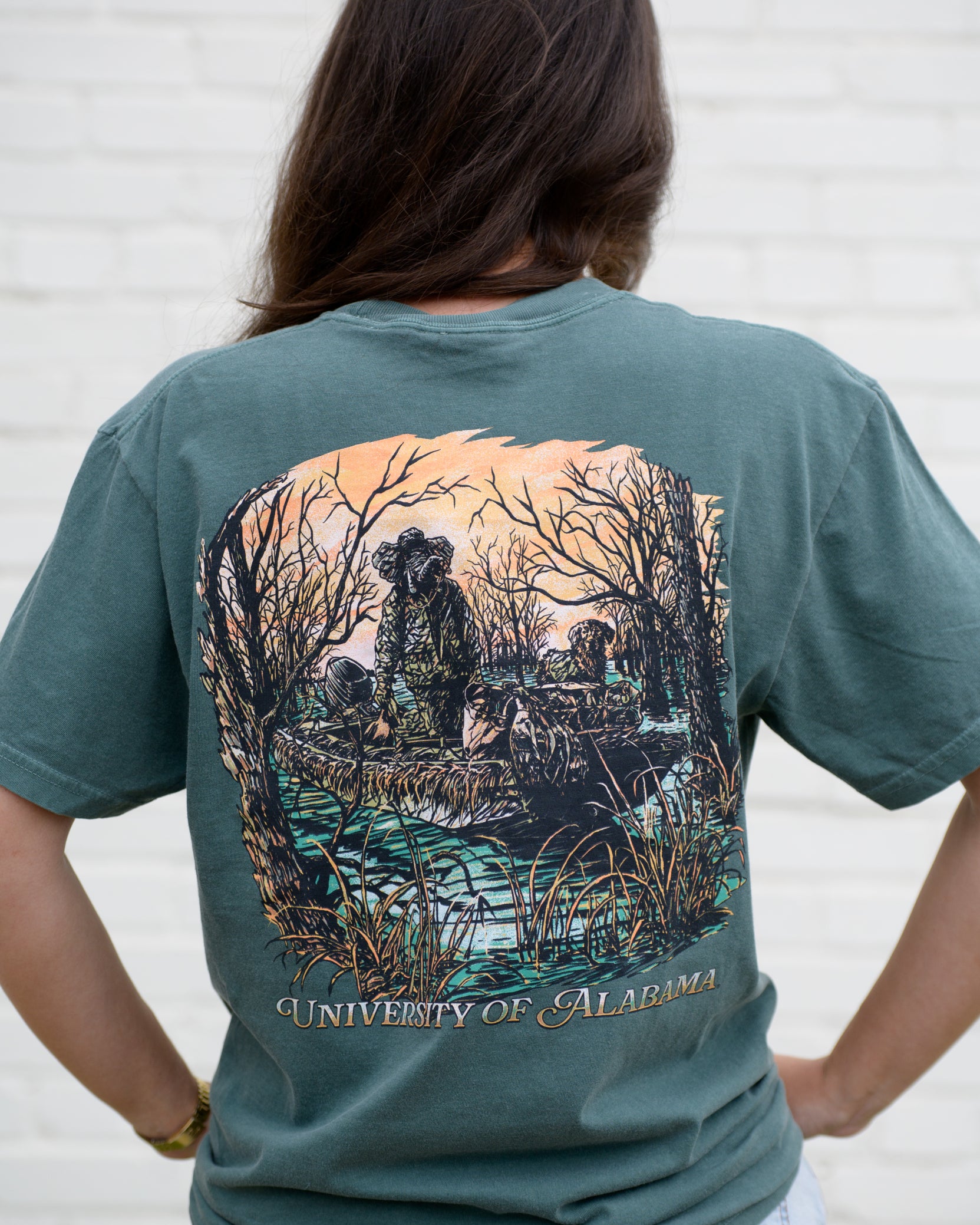 University of Alabama Big Al Duck Hunt Blue Spruce Comfort Colors T-Shirt with an image of Big Al wearing hunting gear with a dog in a boat in the swamp
