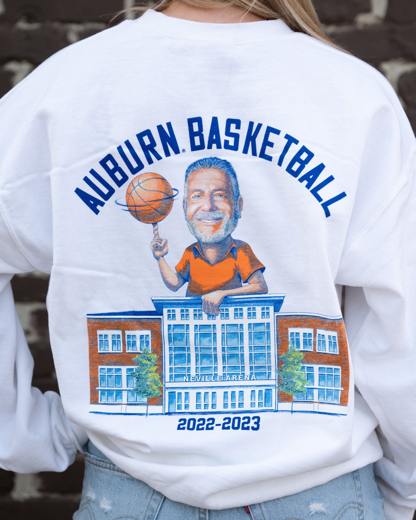 Auburn University White Bruce Pearl 2023 Gildan Sweatshirt with Navy text "Auburn Basketball" above an image of Auburn Basketball Coach Bruce Pearl spinning a basketball and leaning on the basketball building
