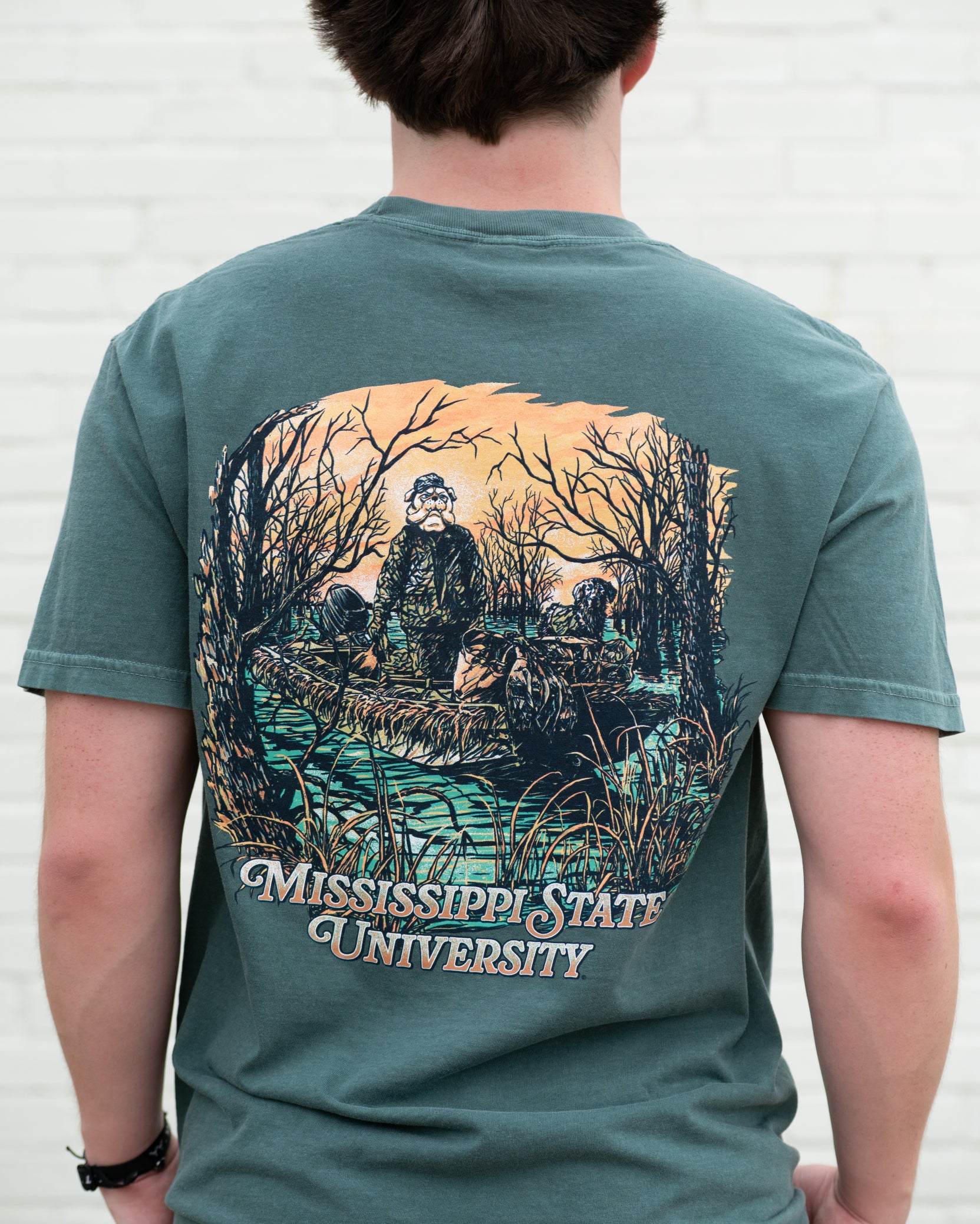 Mississippi State Dark Green T-Shirt with an image of Bully wearing hunting gear with a dog in a boat in the swamp
