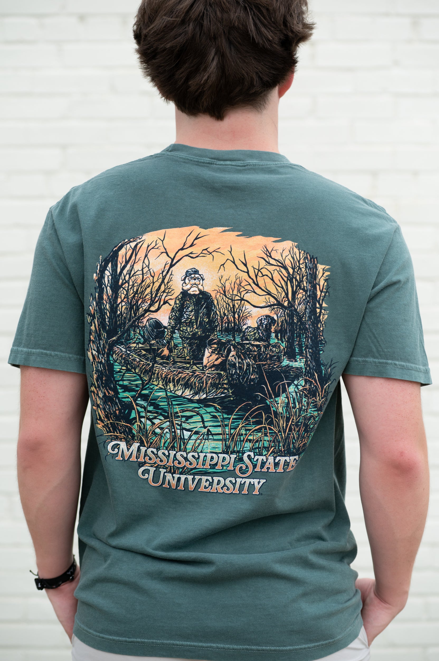 Mississippi State Dark Green T-Shirt with an image of Bully wearing hunting gear with a dog in a boat in the swamp