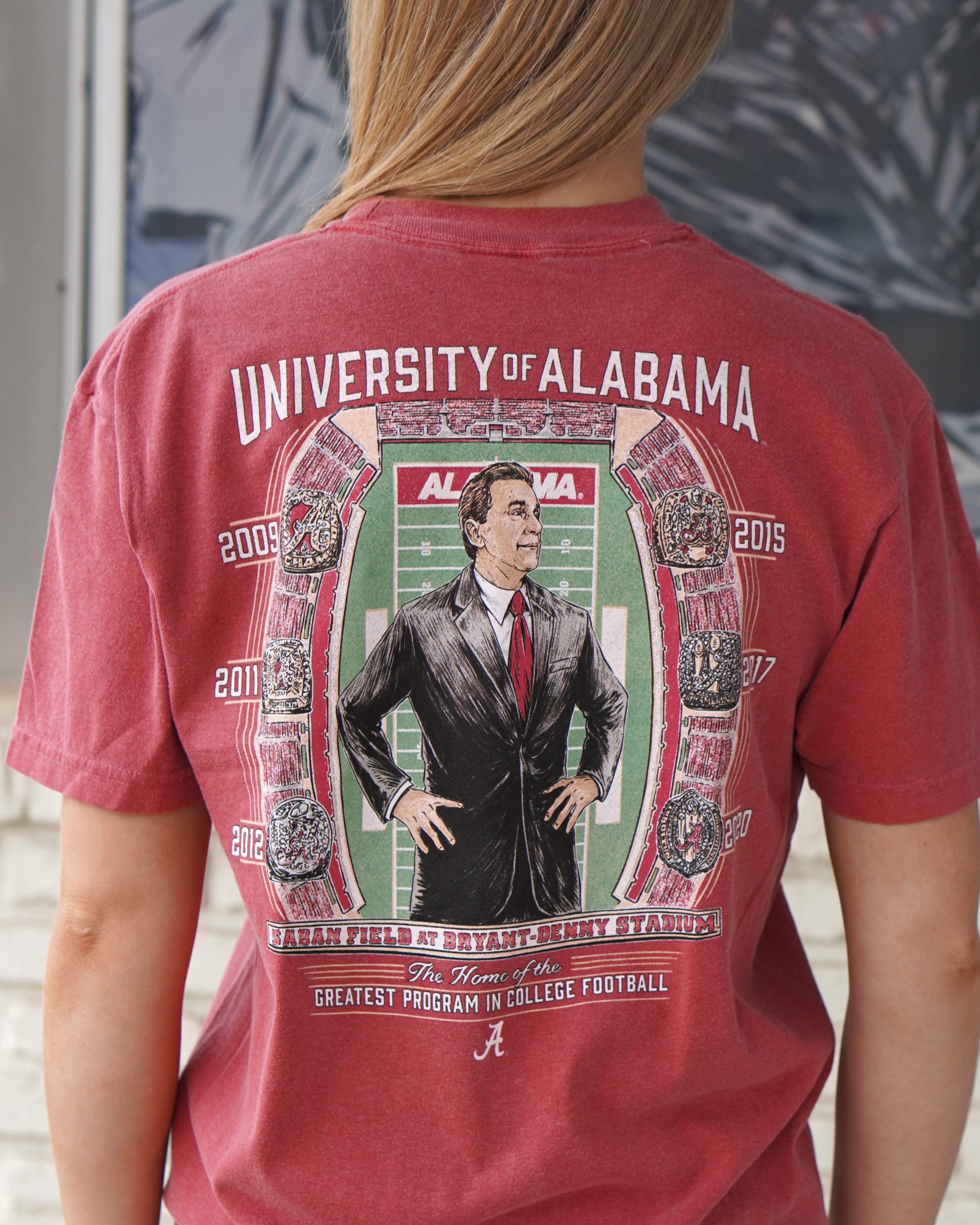 University of Alabama Champion Legacy at Saban Field Red Comfort Colors T-Shirt with an image of Nick Saban standing over Bryant-Denny Stadium surrounded by the years Alabama won the Football Championship