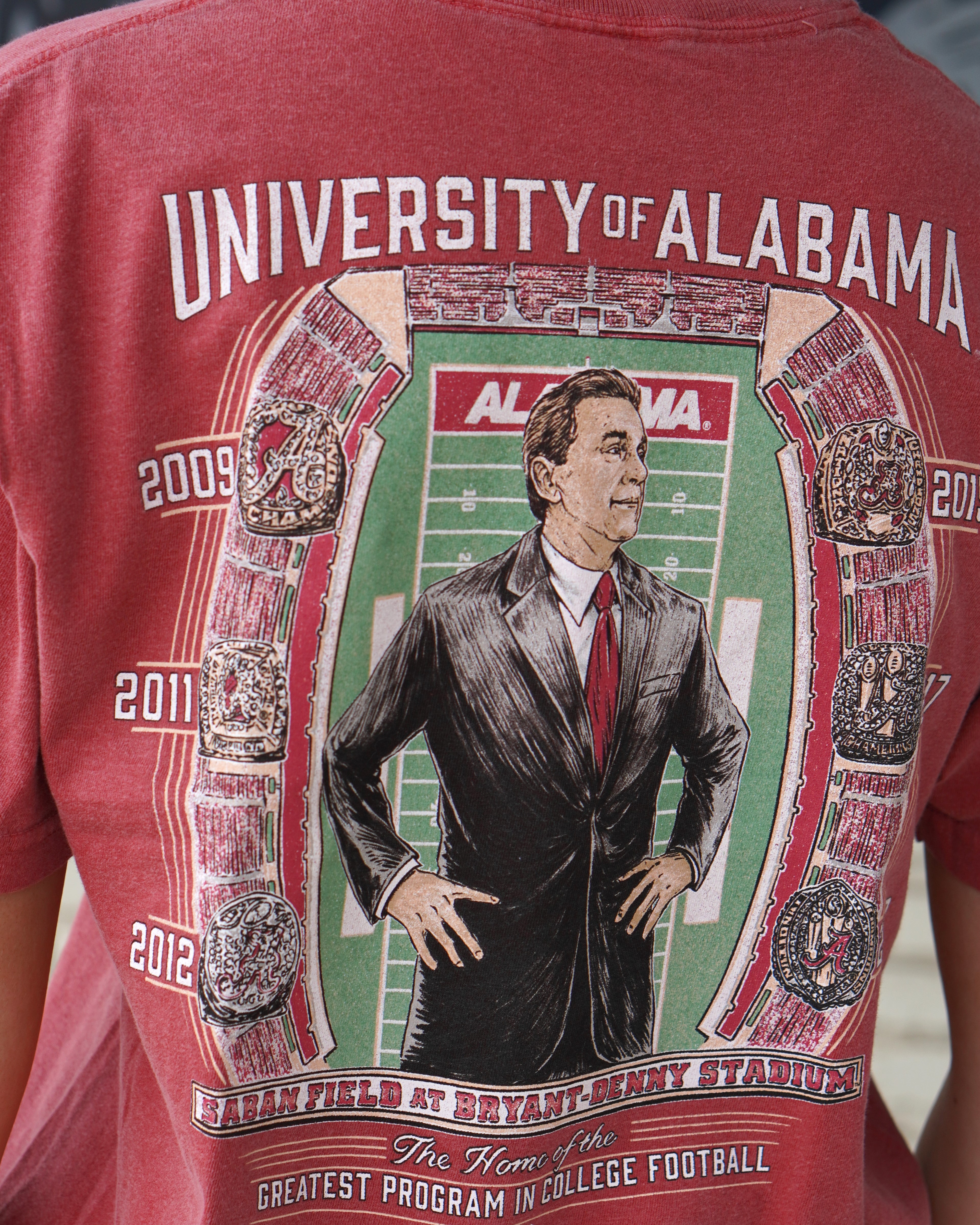 University of Alabama Champion Legacy at Saban Field Red Comfort Colors T-Shirt with an image of Nick Saban standing over Bryant-Denny Stadium surrounded by the years Alabama won the Football Championship