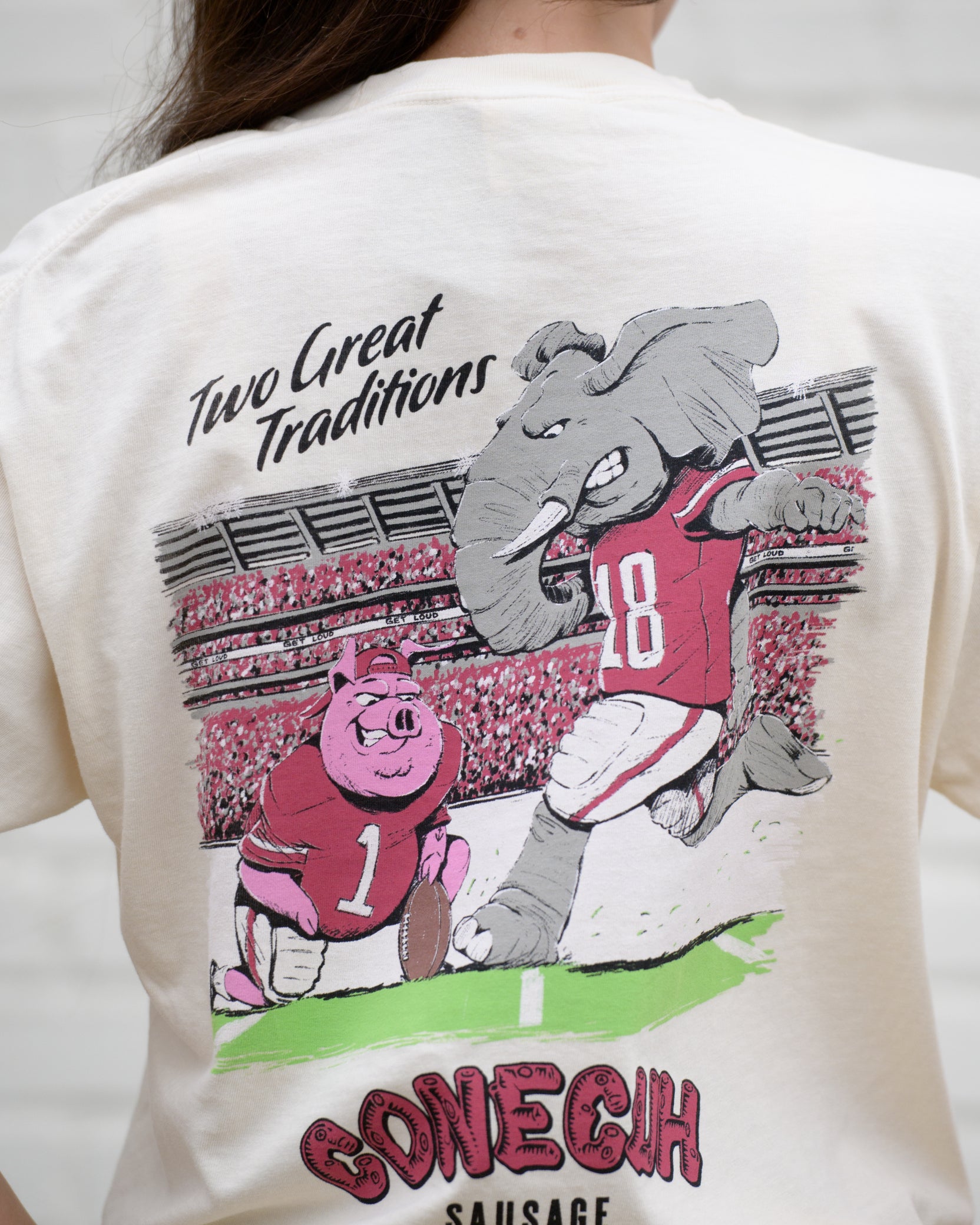 University of Alabama Conecuh Traditions Ivory Comfort Colors T-Shirt with Black text "Two Great Traditions" above an illustration of a pig holding a football for Big Al to kick
