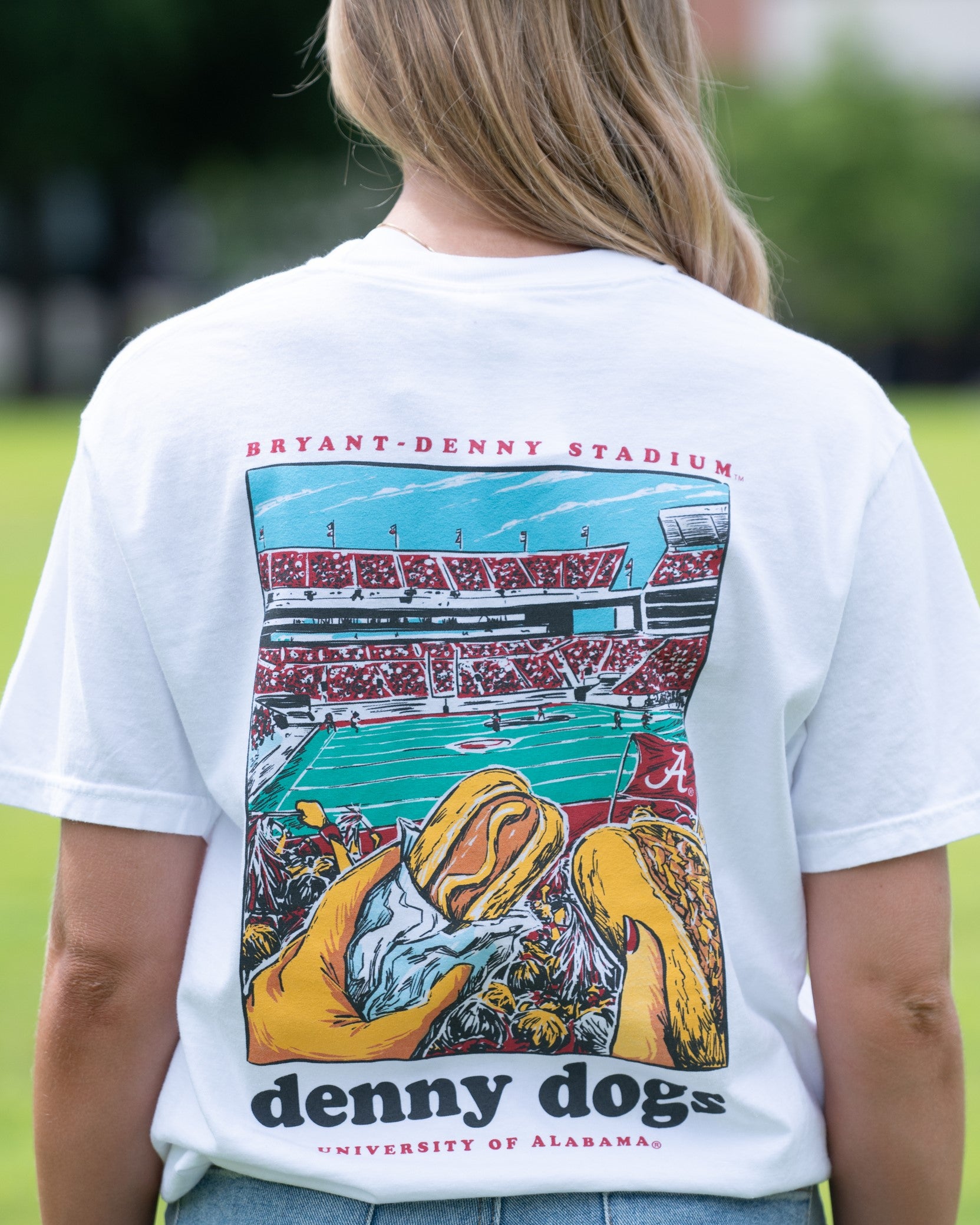 University of Alabama White Denny Dogs Comfort Colors T-Shirt with an image of two hands holding hot dogs at Bryant- Denny Stadium above the Black text "denny dogs"