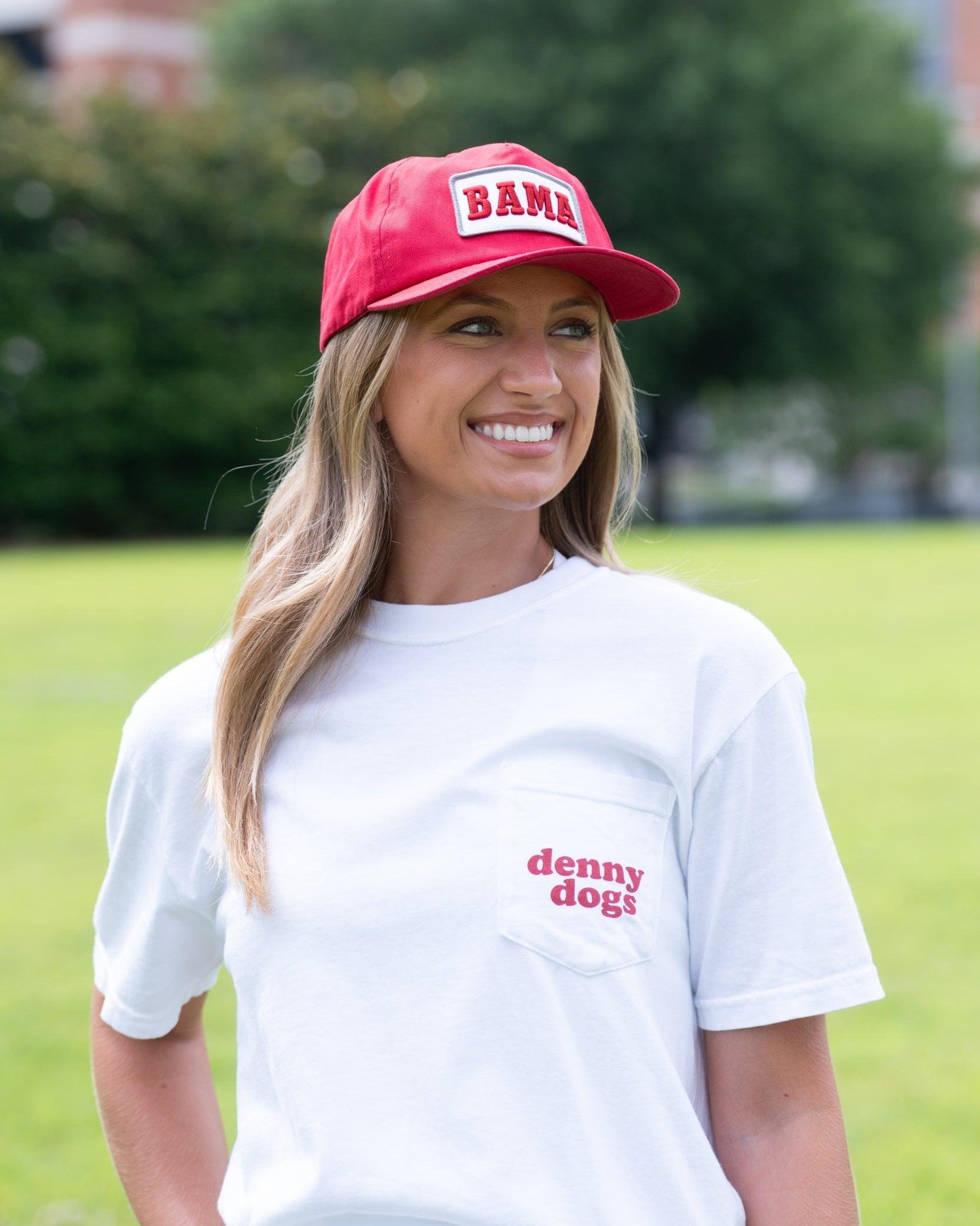 University of Alabama White Denny Dogs Comfort Colors T-Shirt with an image of two hands holding hot dogs at Bryant- Denny Stadium above the Black text "denny dogs"