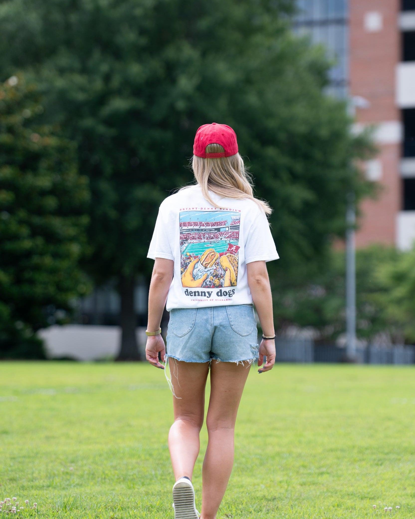 University of Alabama White Denny Dogs Comfort Colors T-Shirt with an image of two hands holding hot dogs at Bryant- Denny Stadium above the Black text "denny dogs"