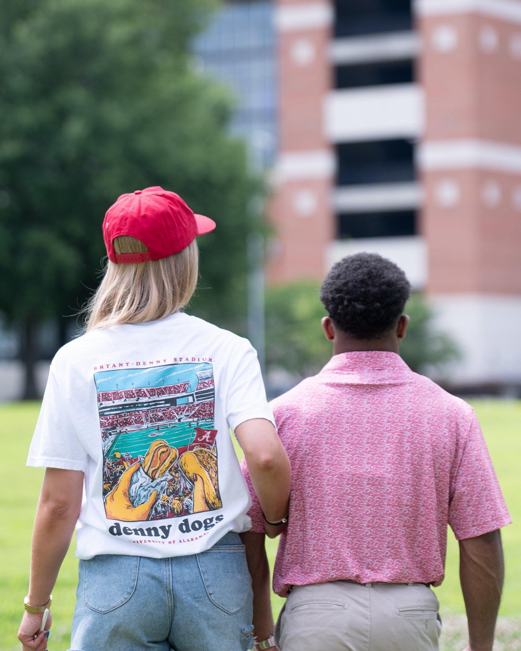 University of Alabama White Denny Dogs Comfort Colors T-Shirt with an image of two hands holding hot dogs at Bryant- Denny Stadium above the Black text "denny dogs"
