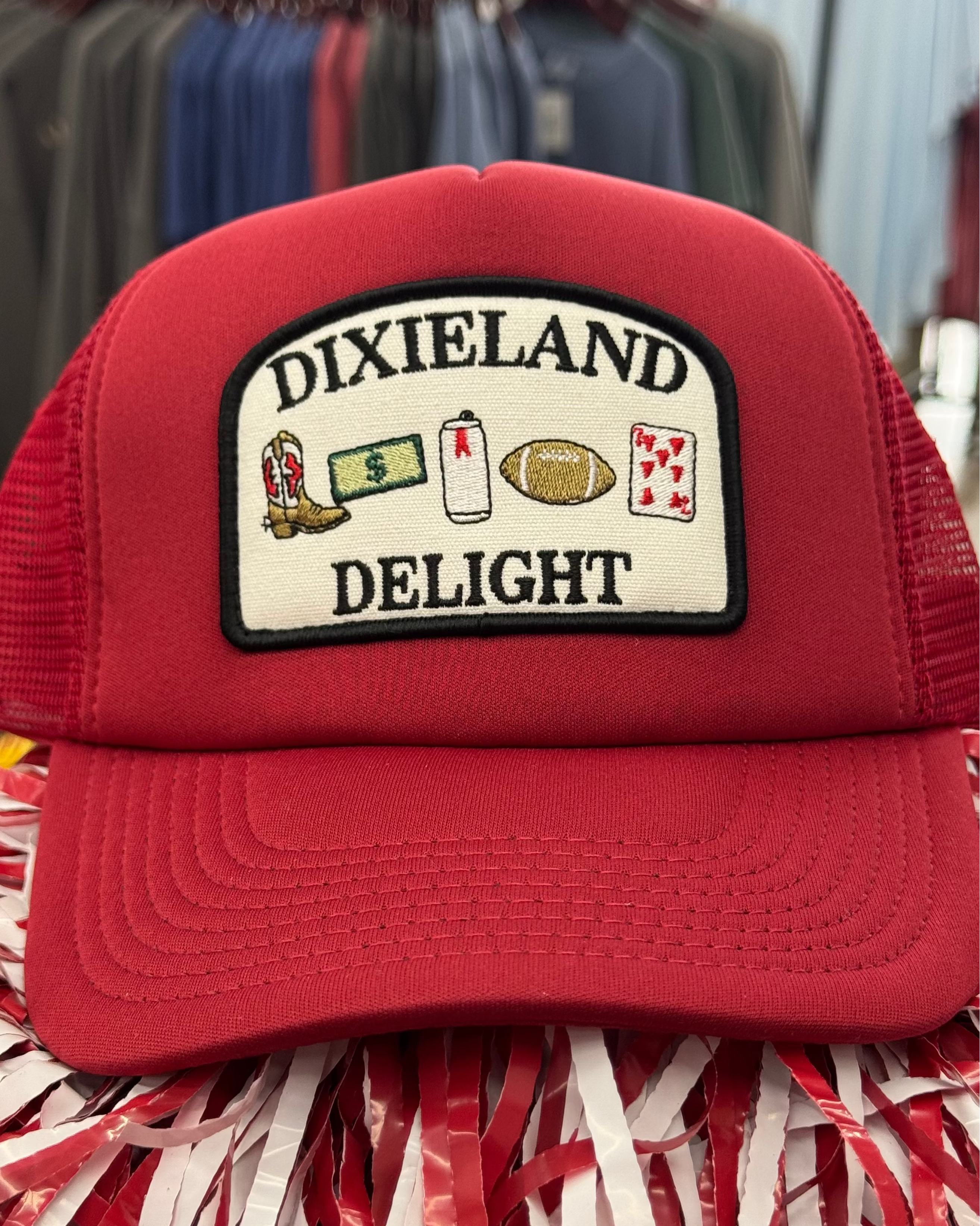 University of Alabama Red Trucker Hat with a patch featuring text “Dixieland” above and “Delight” below drawings of a cowboy boot, money, drink can, football, and playing card