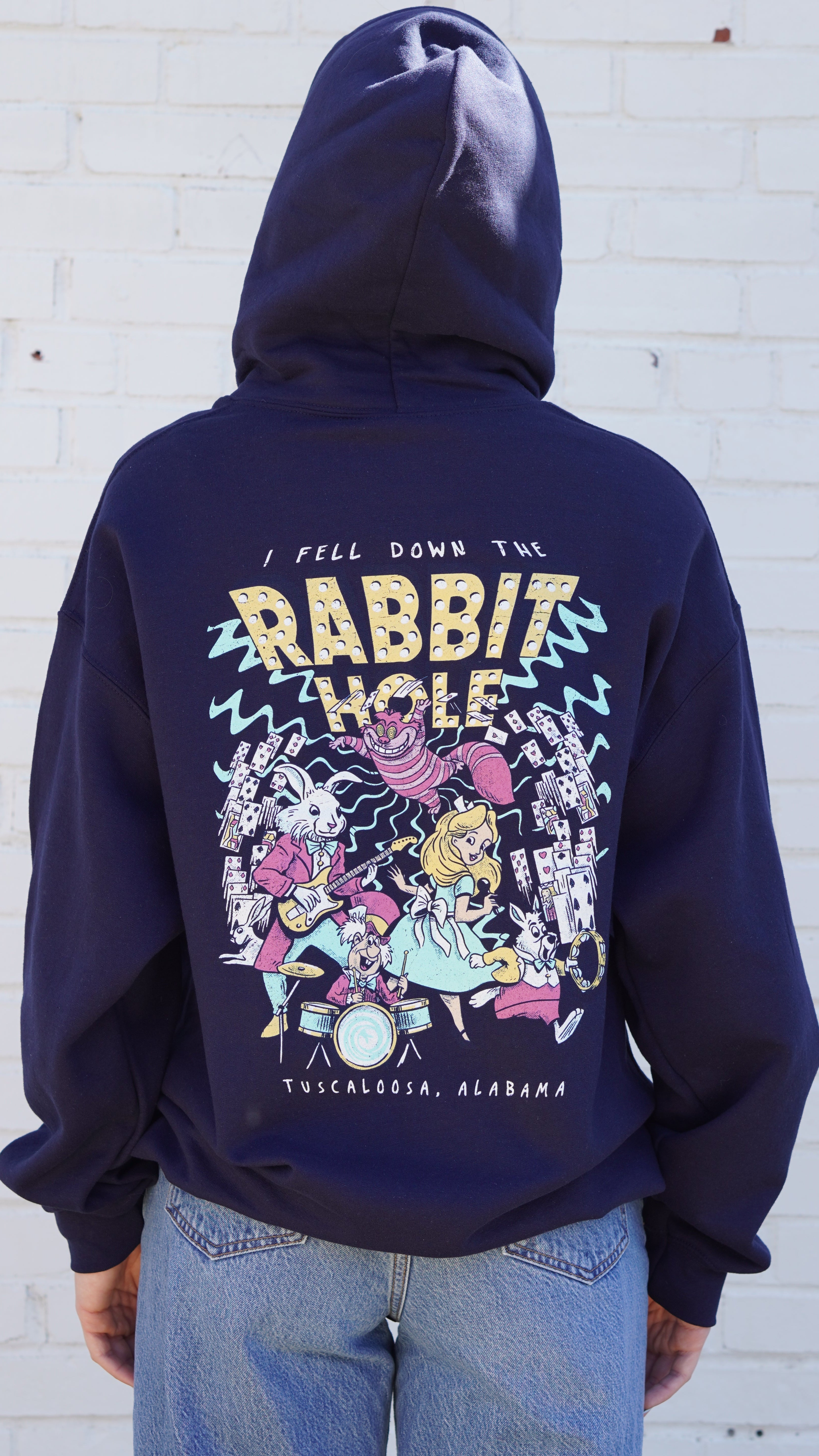 Navy Rabbit Hole Hoodie with marquee lights spelling "Rabbit Hole" lighting a band of Alice in Wonderland characters surrounded by playing cards