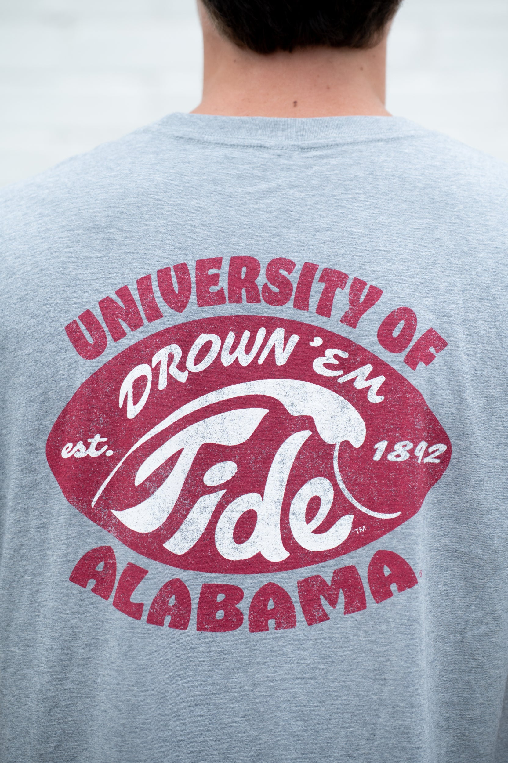 University of Alabama Gray T-Shirt with a Red football shape with a White outline of a tidal wave and White text "Drown 'Em Tide"