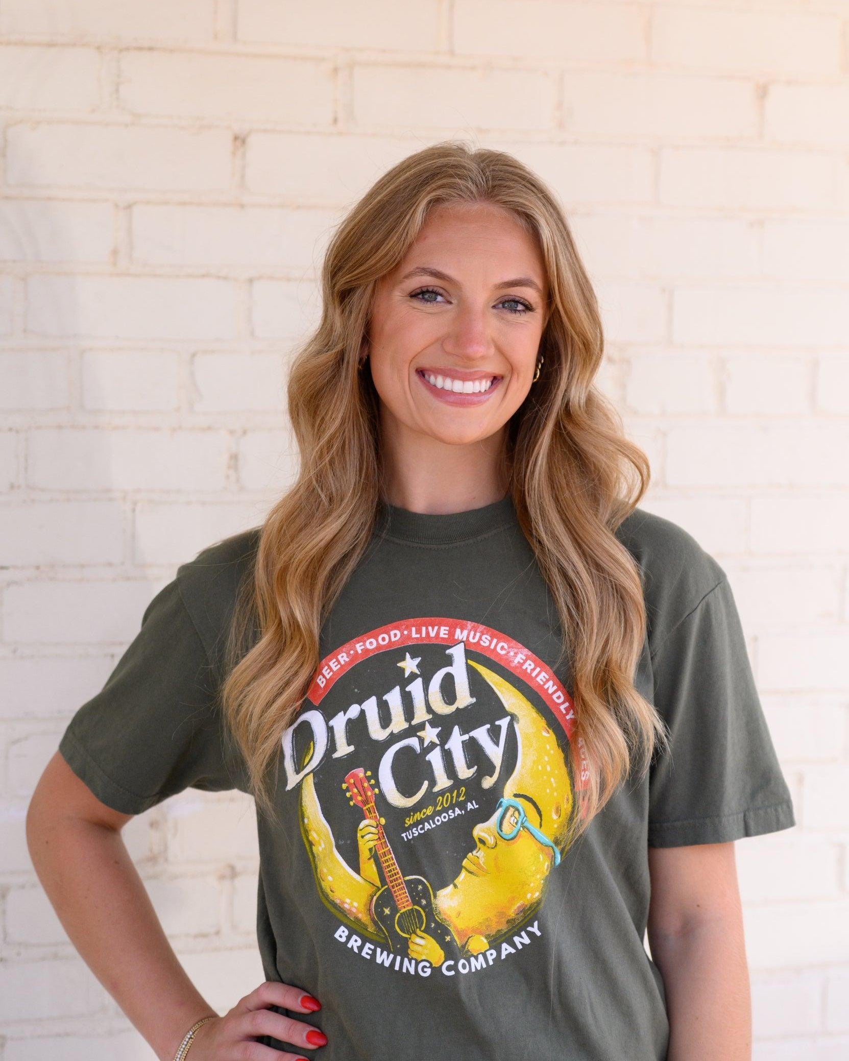 Druid City Brewing Company Olive Green Tee with text "Druid City" above a Crescent Moon wearing glasses and playing a guitar