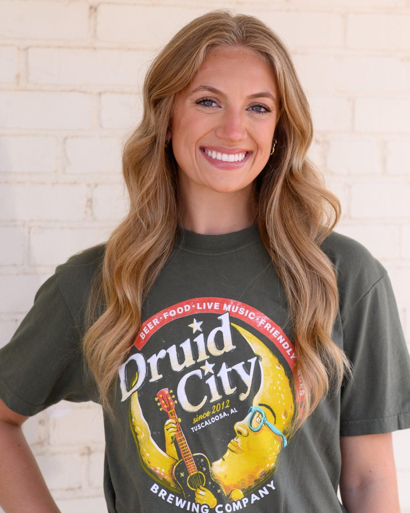 Druid City Brewing Company Olive Green Tee with text "Druid City" above a Crescent Moon wearing glasses and playing a guitar