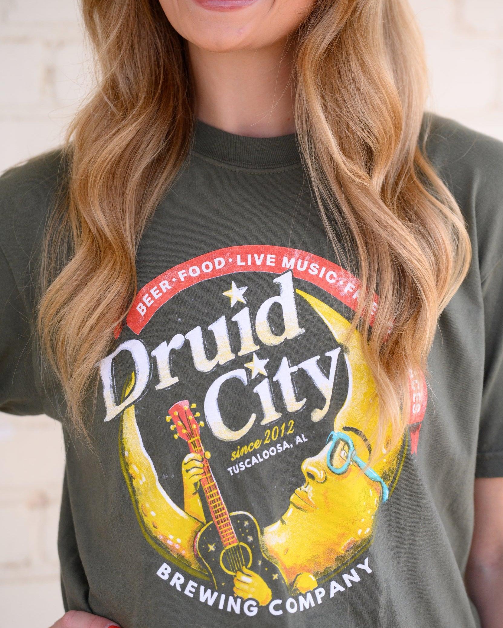 Druid City Brewing Company Olive Green Tee with text "Druid City" above a Crescent Moon wearing glasses and playing a guitar