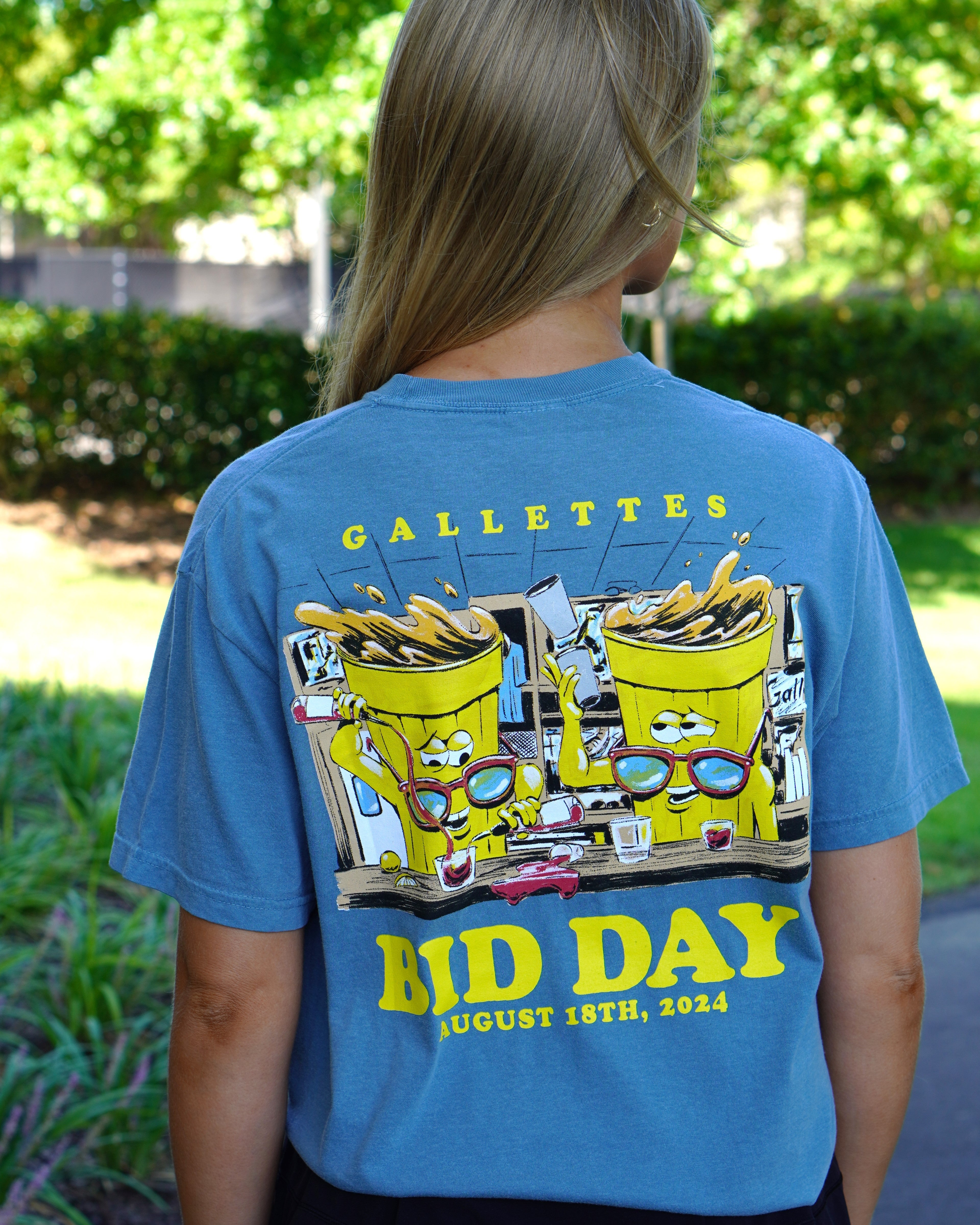 Gallettes Blue Bid Day T-Shirt with two yellow cups wearing sunglasses sitting at a bar and pouring themselves drinks above Yellow text "Bid Day August 18th, 2024"