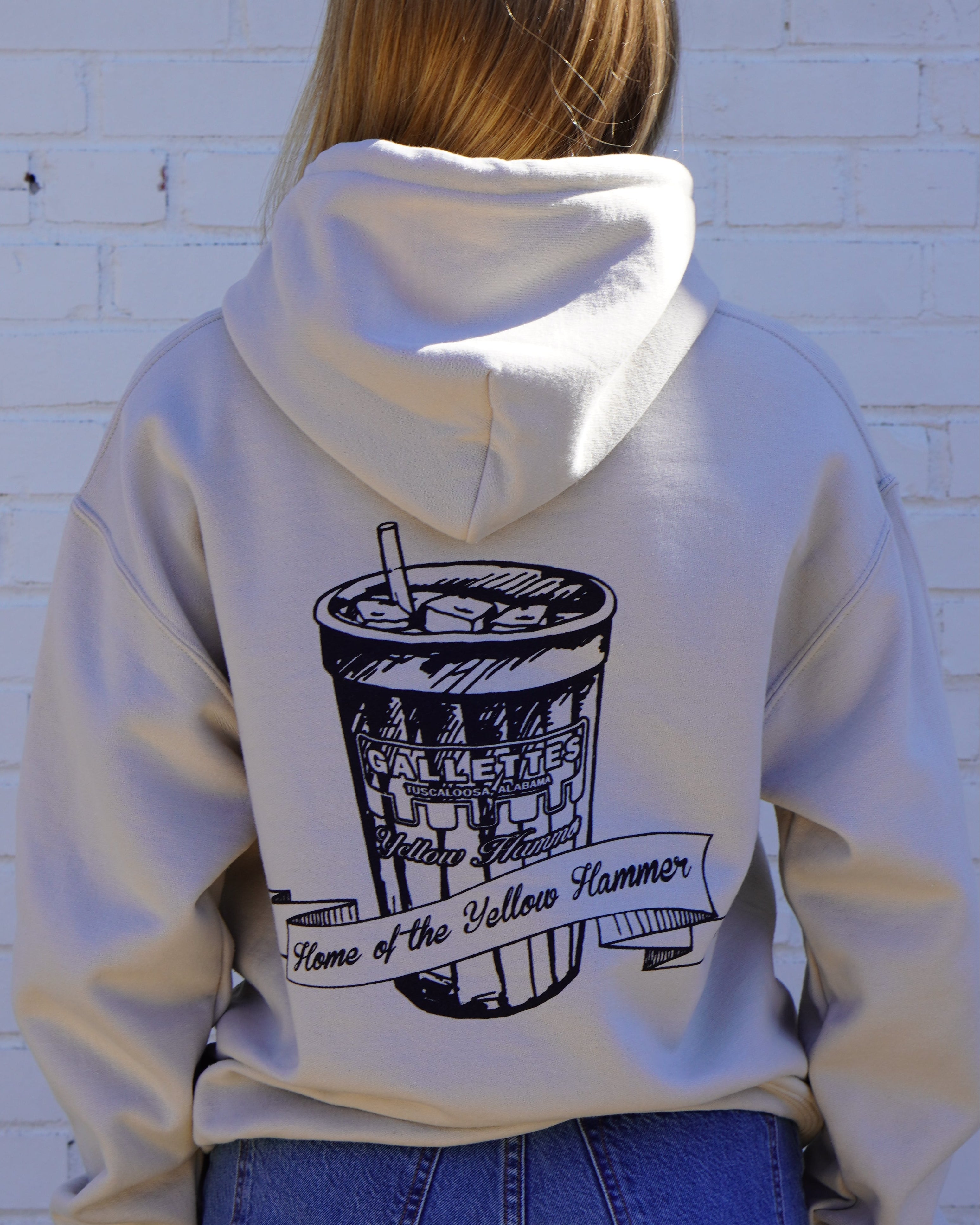 Gallettes Tan Hoodie with an illustration of a yellow hammer drink with a sash that reads “home of the yellow hammer”