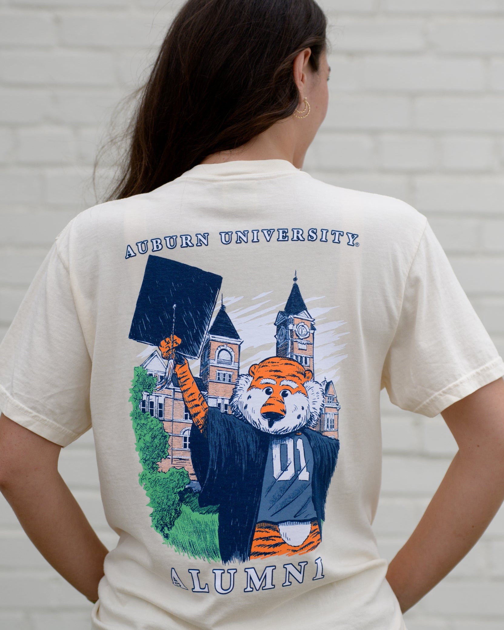 Auburn University Cream Aubie Graduation T-Shirt with an image of Aubie in graduation attire in front of Samford Hall above White text "Alumni”