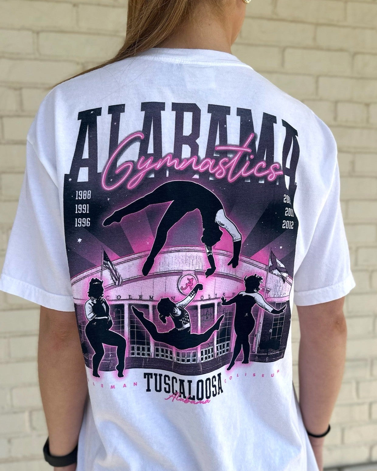 University of Alabama White Ladies' Gymnastics T-Shirt with a hand-drawn design featuring Coleman Coliseum and the years of the Crimson Tide's national titles.