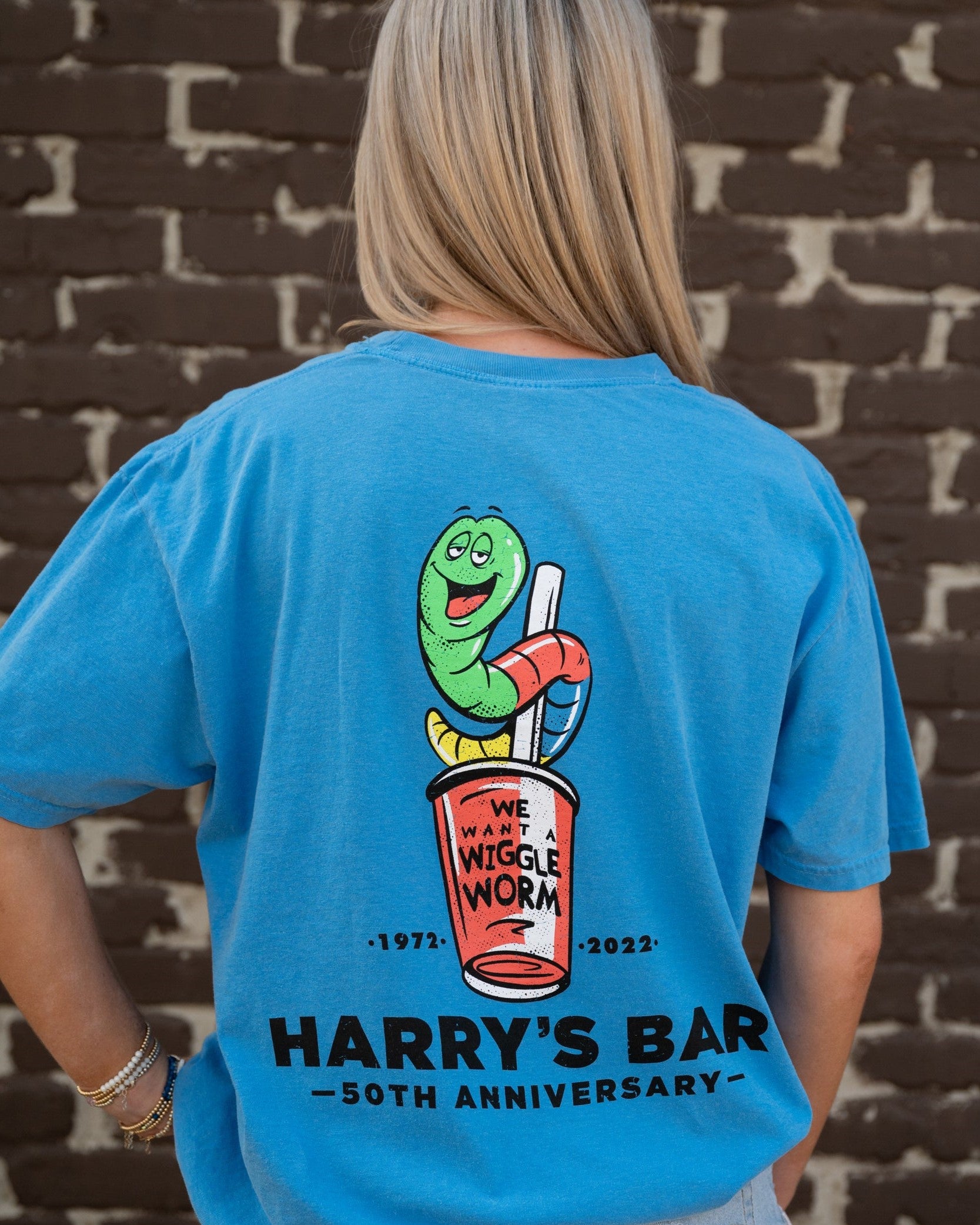 Harry's Bar Blue Shirt with a cartoon of the Wiggle Worm Drink above Black text “Harry’s Bar”