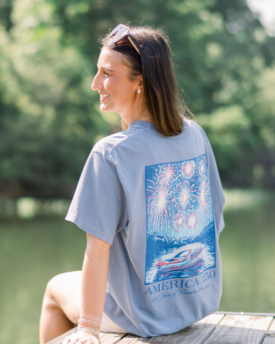 America 250 Blue Jean T-Shirt with impressionist style art of a boat on the lake while fireworks explode above, and text “America 250”
