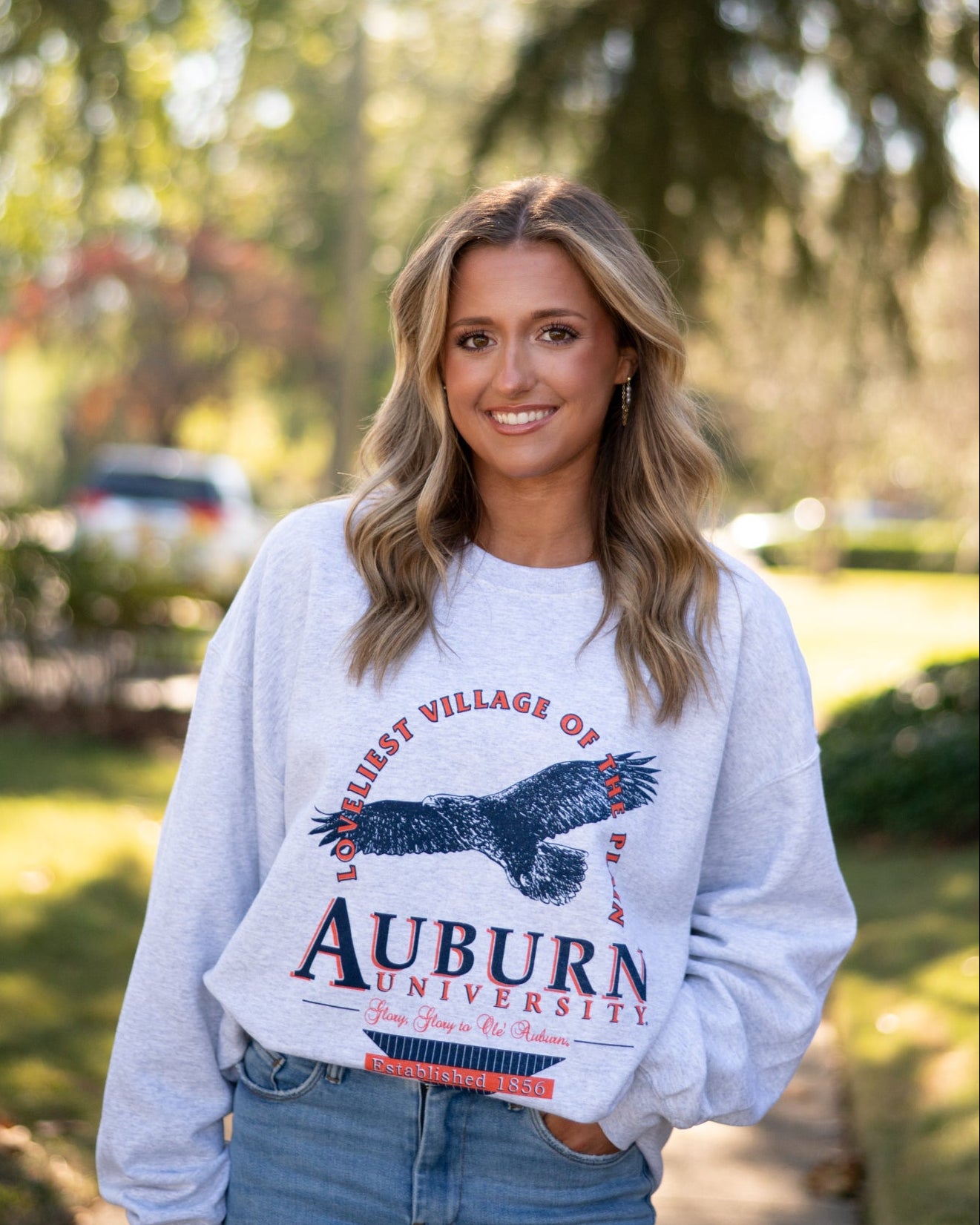 Auburn University Grey Sweatshirt with an image of an eagle flying under Orange text “Loveliest Village of the Plains” and above text “Auburn University”