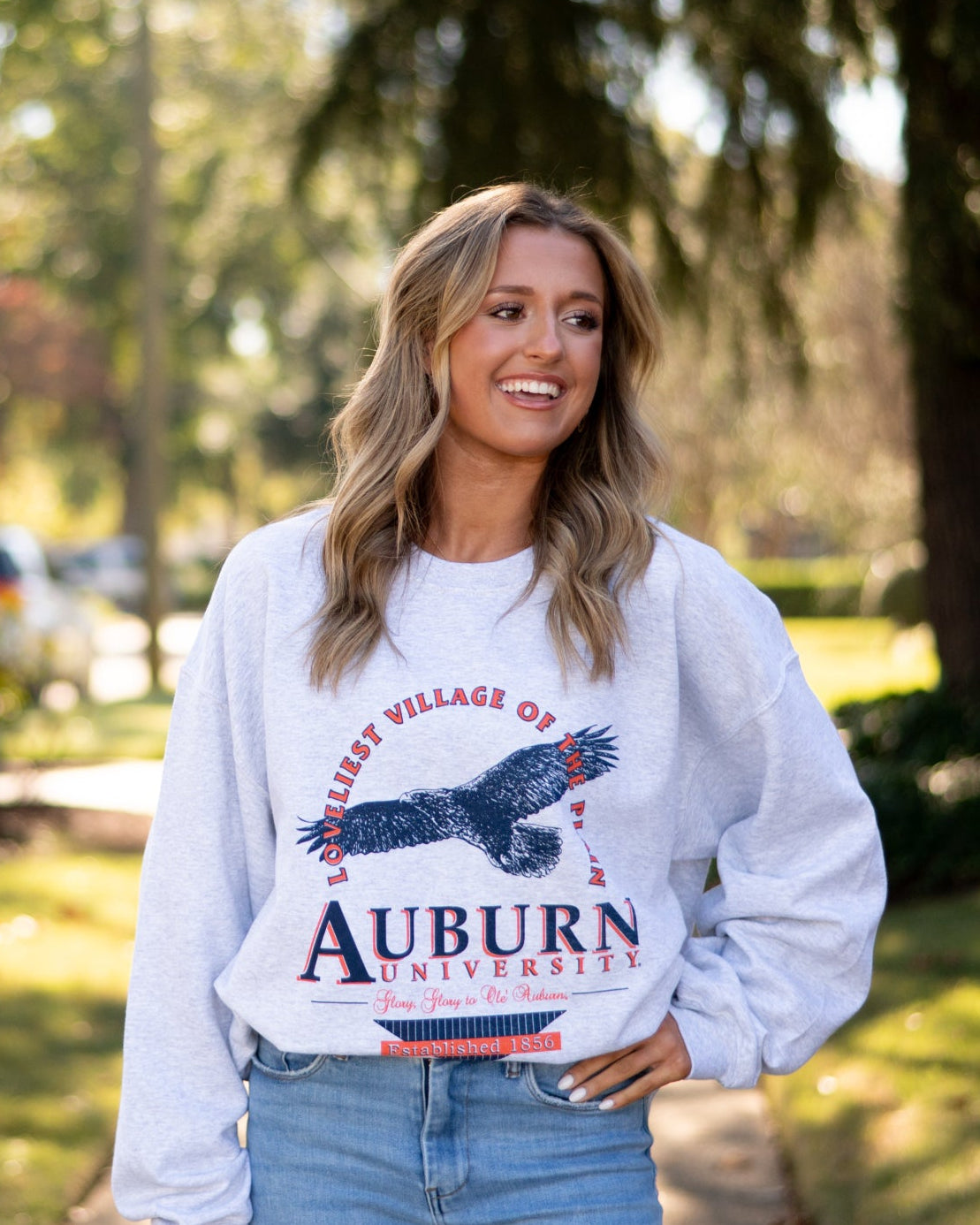 Auburn University Grey Sweatshirt with an image of an eagle flying under Orange text “Loveliest Village of the Plains” and above text “Auburn University”