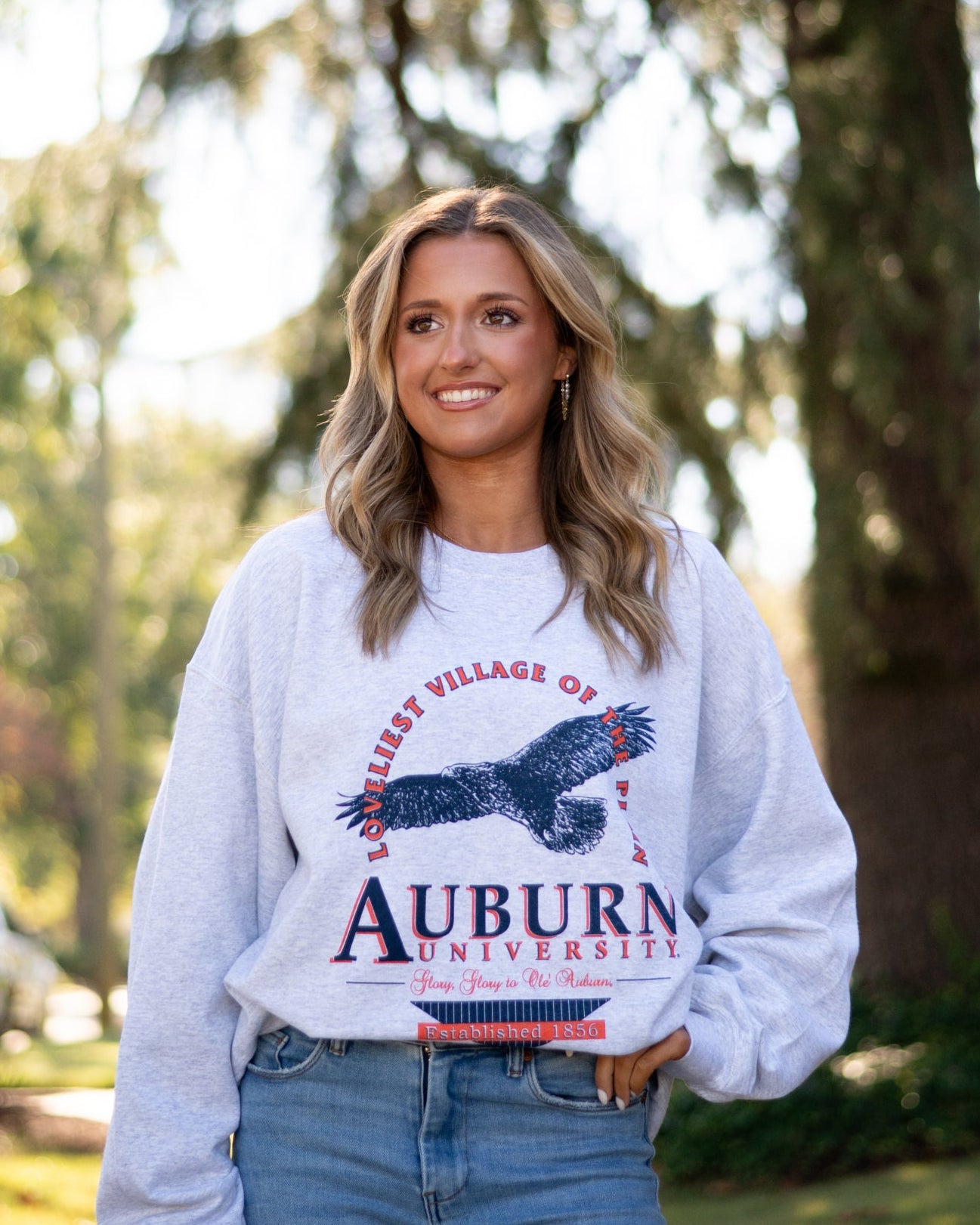 Auburn University Grey Sweatshirt with an image of an eagle flying under Orange text “Loveliest Village of the Plains” and above text “Auburn University”