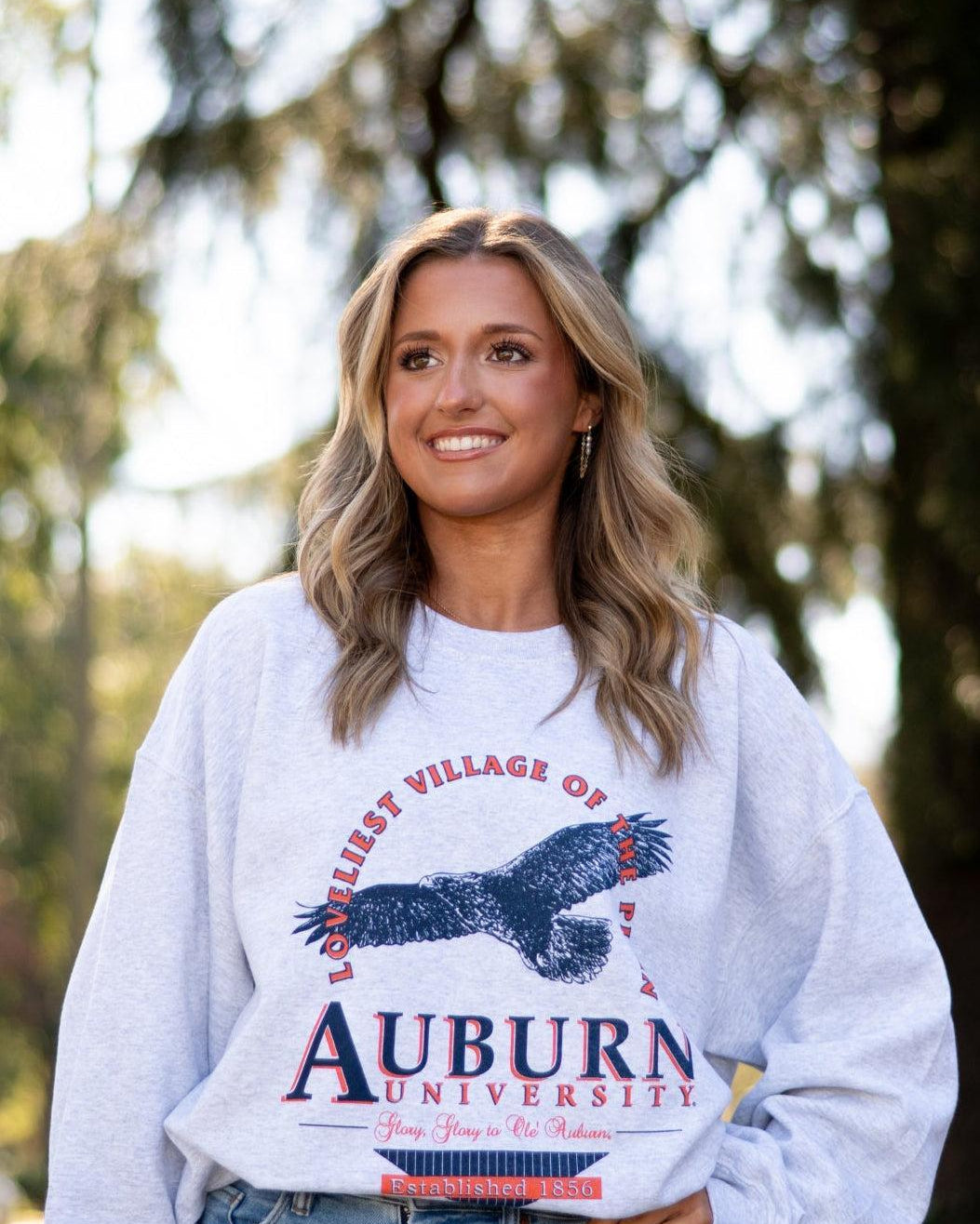 Auburn University Grey Sweatshirt with an image of an eagle flying under Orange text “Loveliest Village of the Plains” and above text “Auburn University”