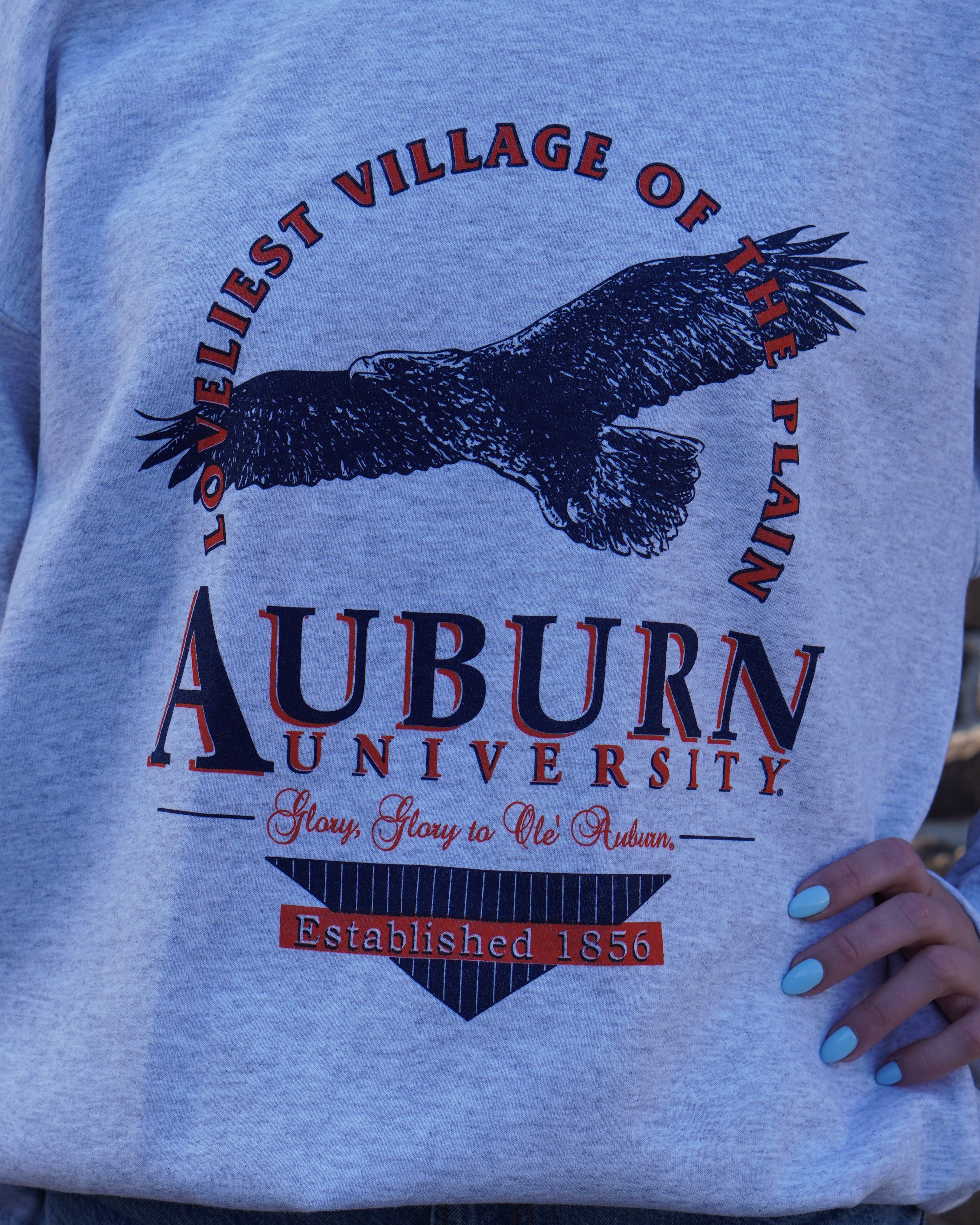 Auburn University Grey Sweatshirt with an image of an eagle flying under Orange text “Loveliest Village of the Plains” and above text “Auburn University”