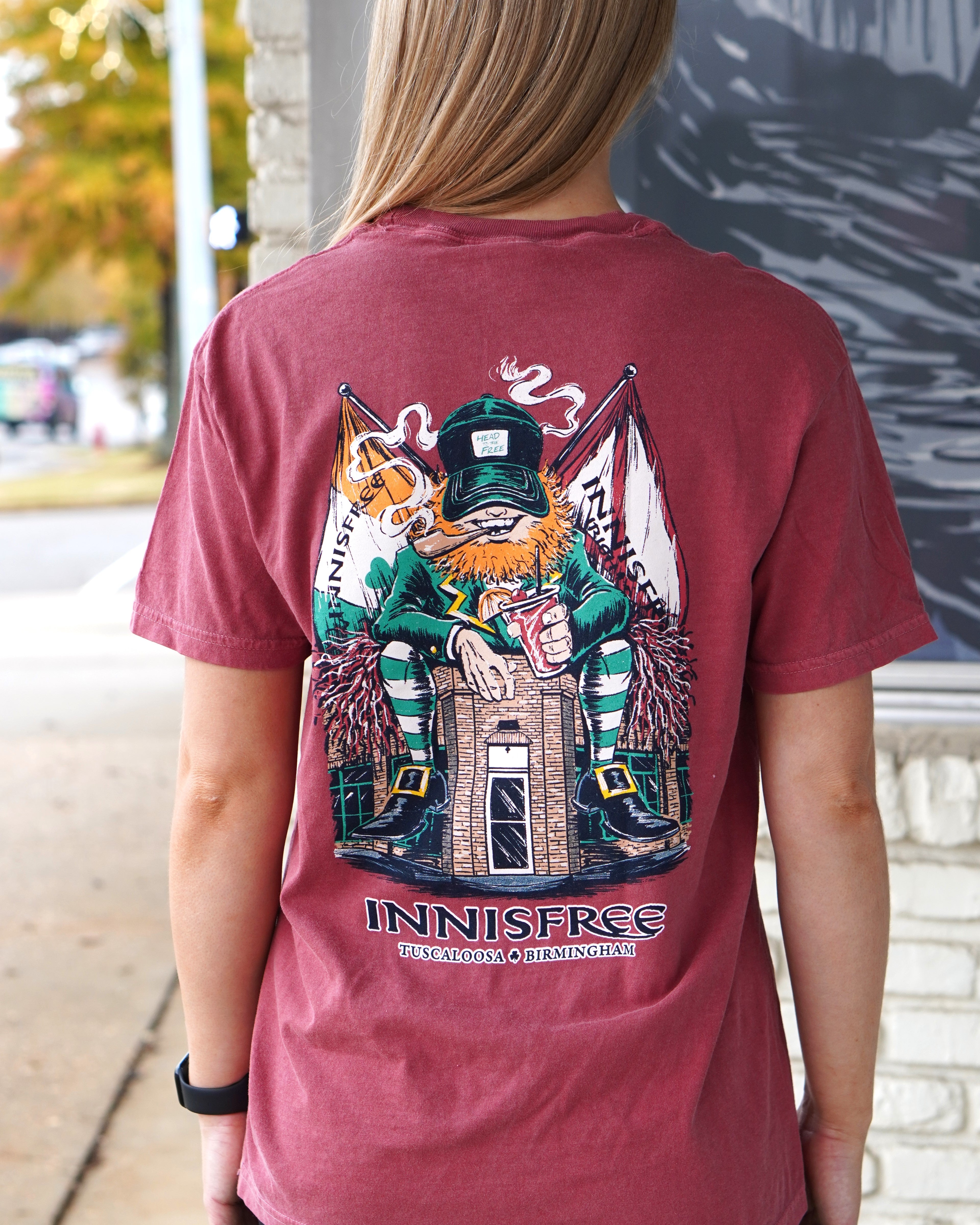 Innisfree Crimson Lucky Leprechaun T-Shirt with an image of a leprechaun sitting on top of the Innisfree Building