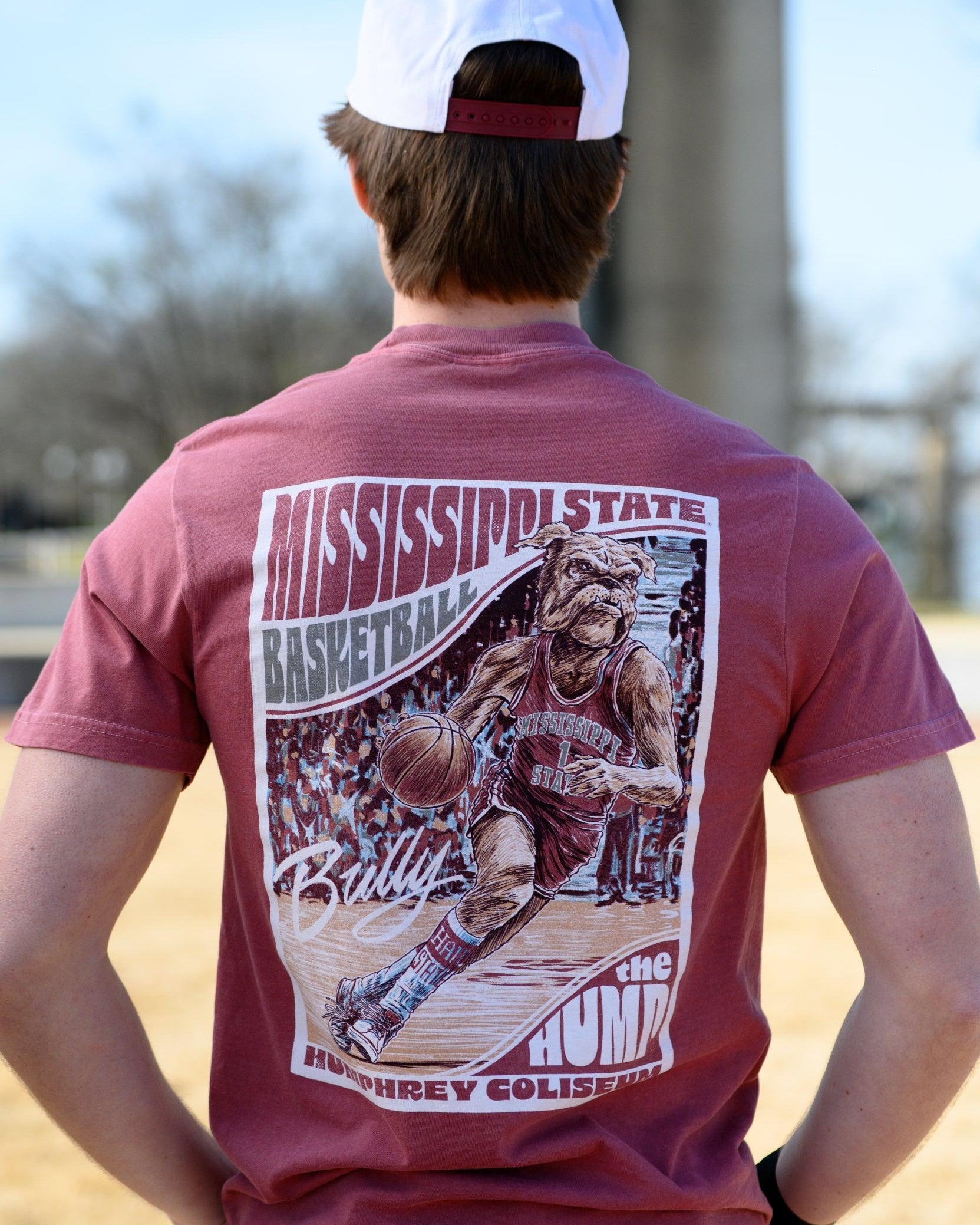 Mississippi State Crimson T-Shirt with a basketball card style design featuring Bully dribbling a basketball down the court in between text “Mississippi State Basketball” and “The Hump Humphrey Coliseum,” and with an autograph from Bully