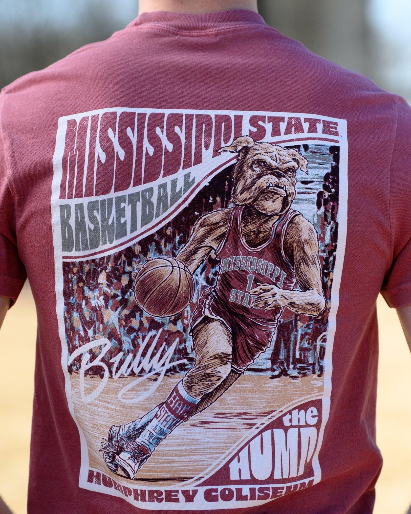 Mississippi State Crimson T-Shirt with a basketball card style design featuring Bully dribbling a basketball down the court in between text “Mississippi State Basketball” and “The Hump Humphrey Coliseum,” and with an autograph from Bully