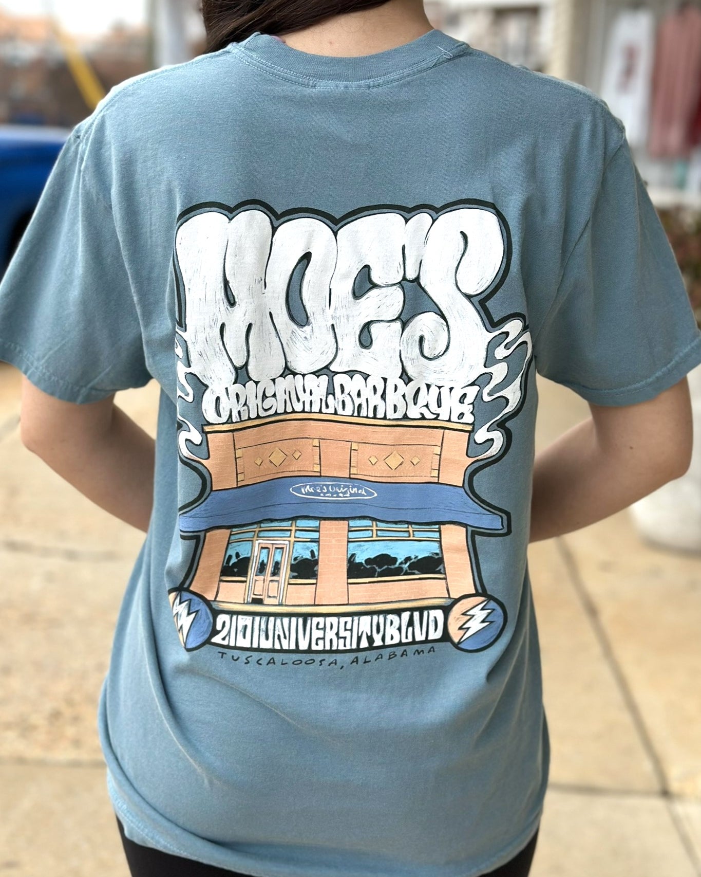 Moe's Ice Blue T-Shirt with White text "Moe's Original Barbeque" above an illustration of the Moe's Building