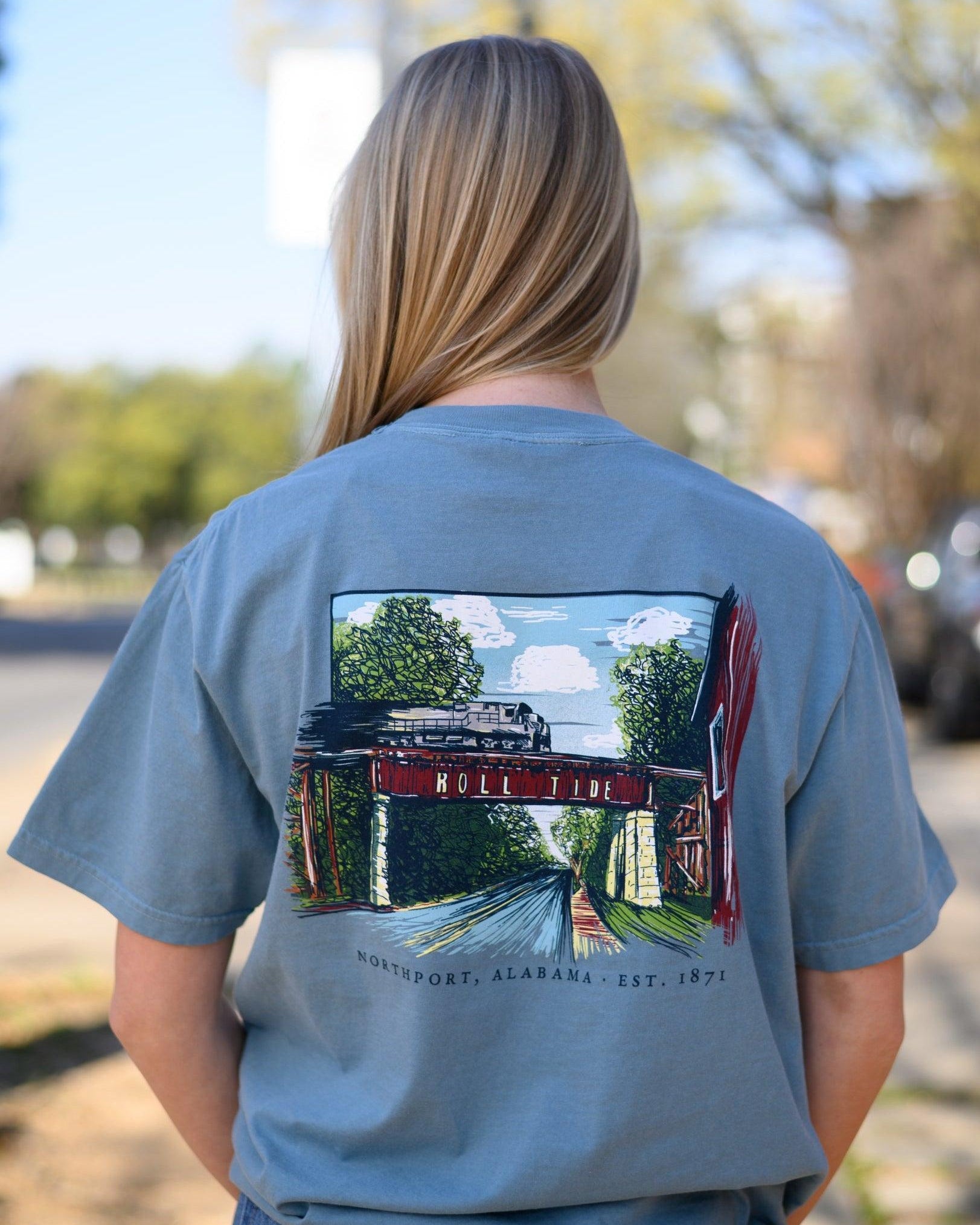 Local Merch Dusty Blue T-Shirt with a hand-drawn illustration of the Downtown Northport Train tracks above Black text "Northport, Alabama EST. 1871"