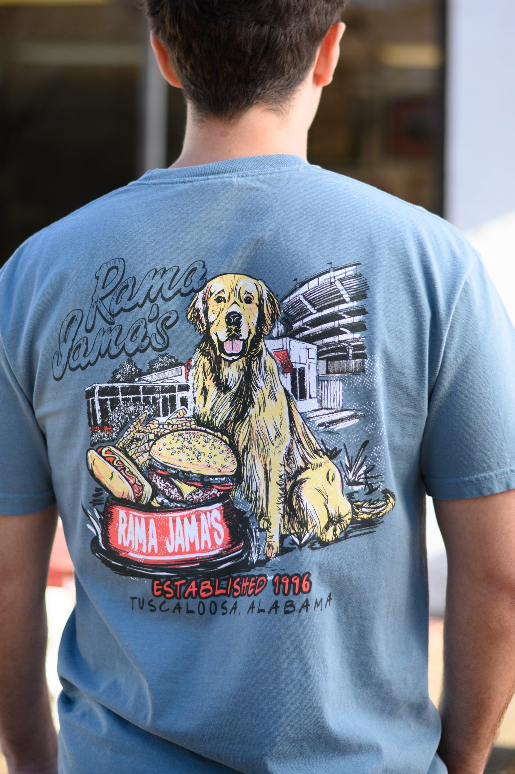 Rama Jama’s Dusty Blue shirt with an illustration of a golden retriever sitting at the picnic tables outside of the building with a cheeseburger and a hotdog