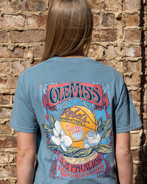 Ole Miss Dusty Light Blue T-Shirt with a basketball card style design featuring a basketball with magnolia flowers in between text “Ole Miss” and “SJB Pavilion”