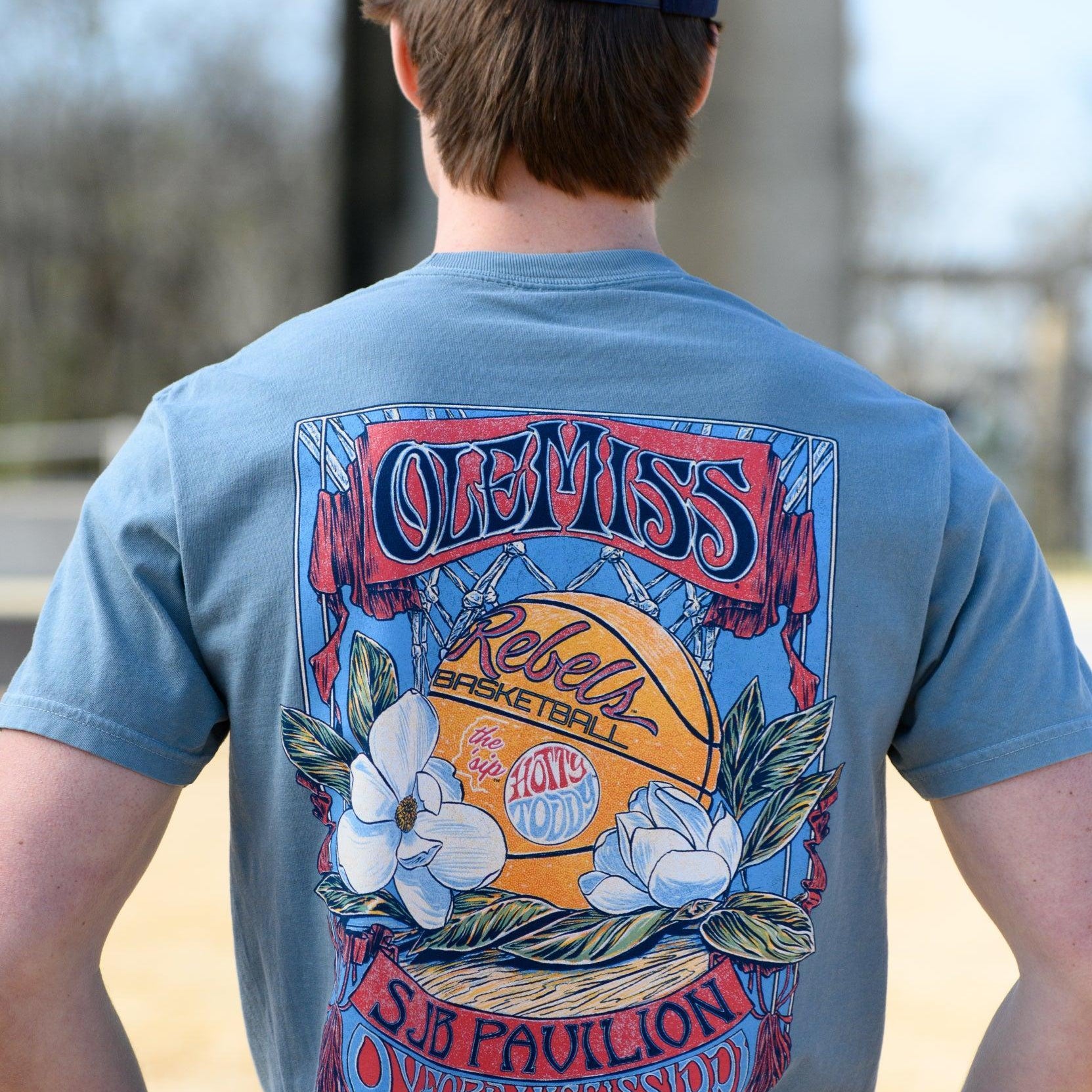 Ole Miss Dusty Light Blue T-Shirt with a basketball card style design featuring a basketball with magnolia flowers in between text “Ole Miss” and “SJB Pavilion”